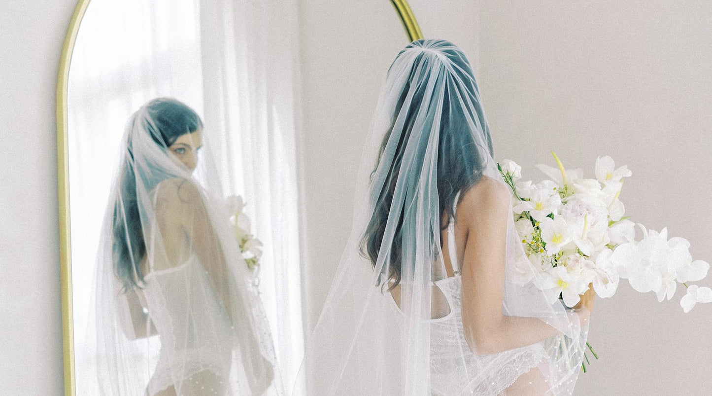 A bride standing in front of a mirror wearing a wedding veil