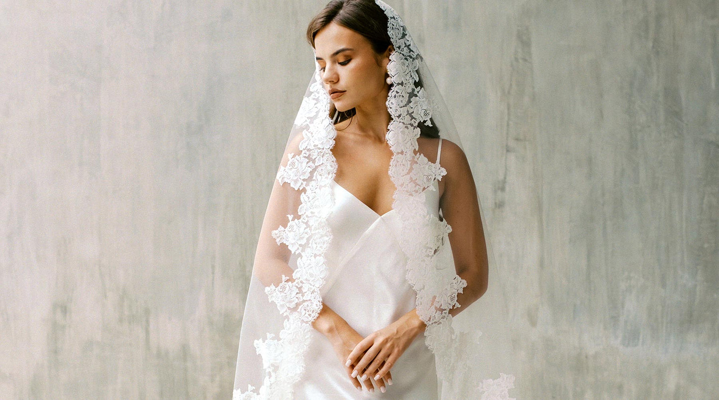 A bride wearing a simple white gown and a beautiful lace mantilla veil by Madame Tulle bridal