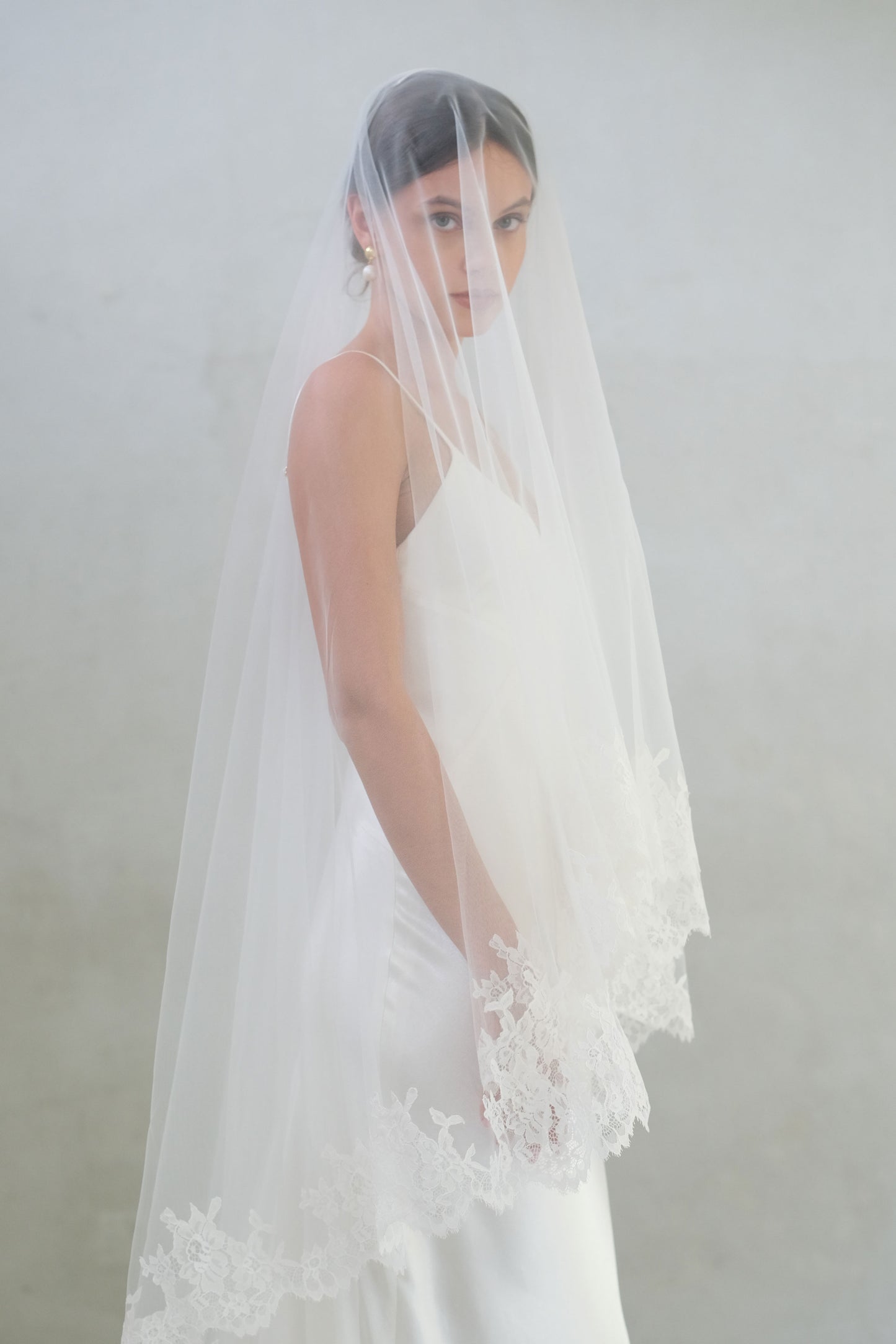 Half length side view of long laced edged wedding veil worn with blusher down
