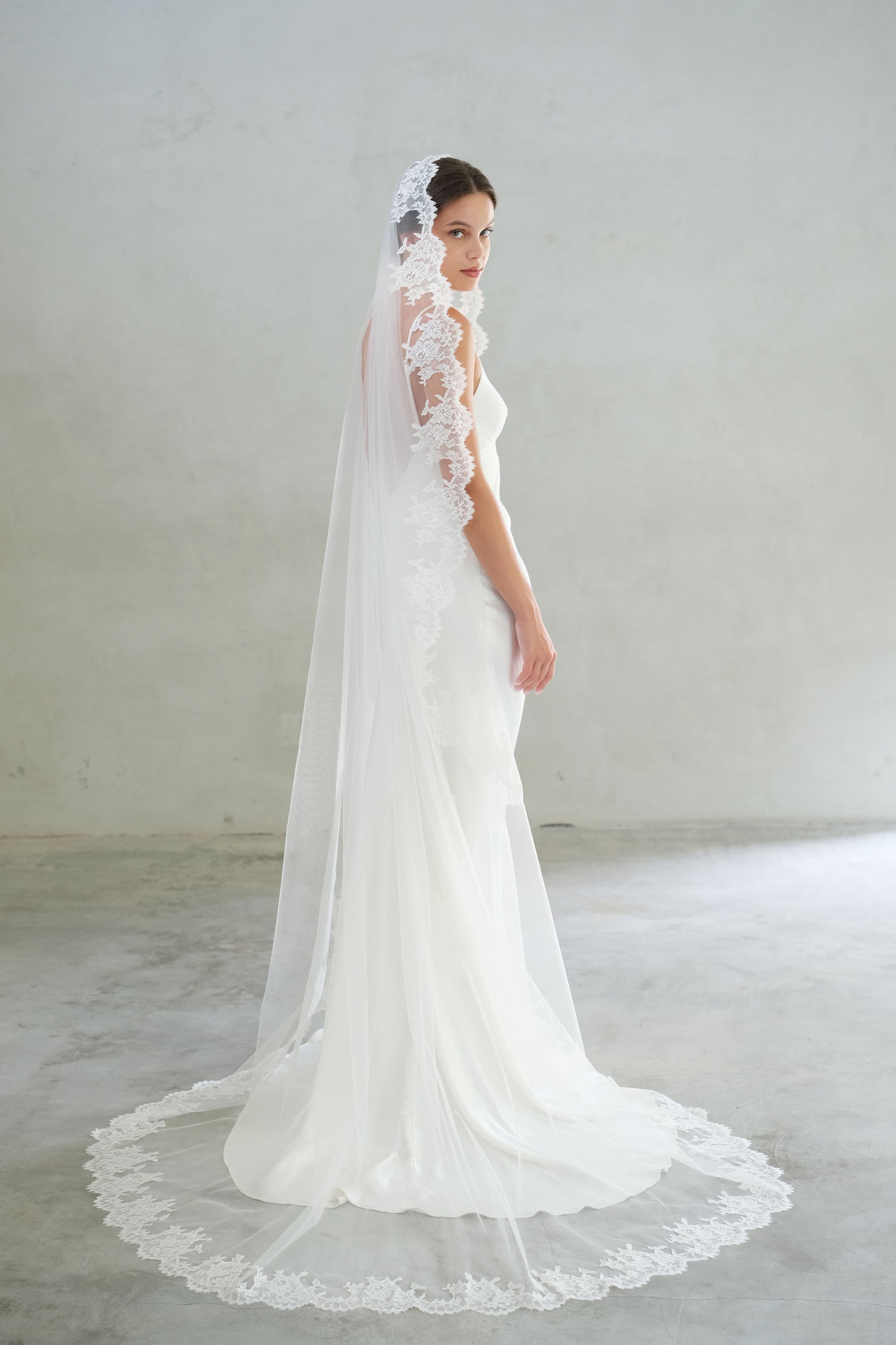 Full length bride turns to show chapel length mantilla veil with floral lace trim on edges and train