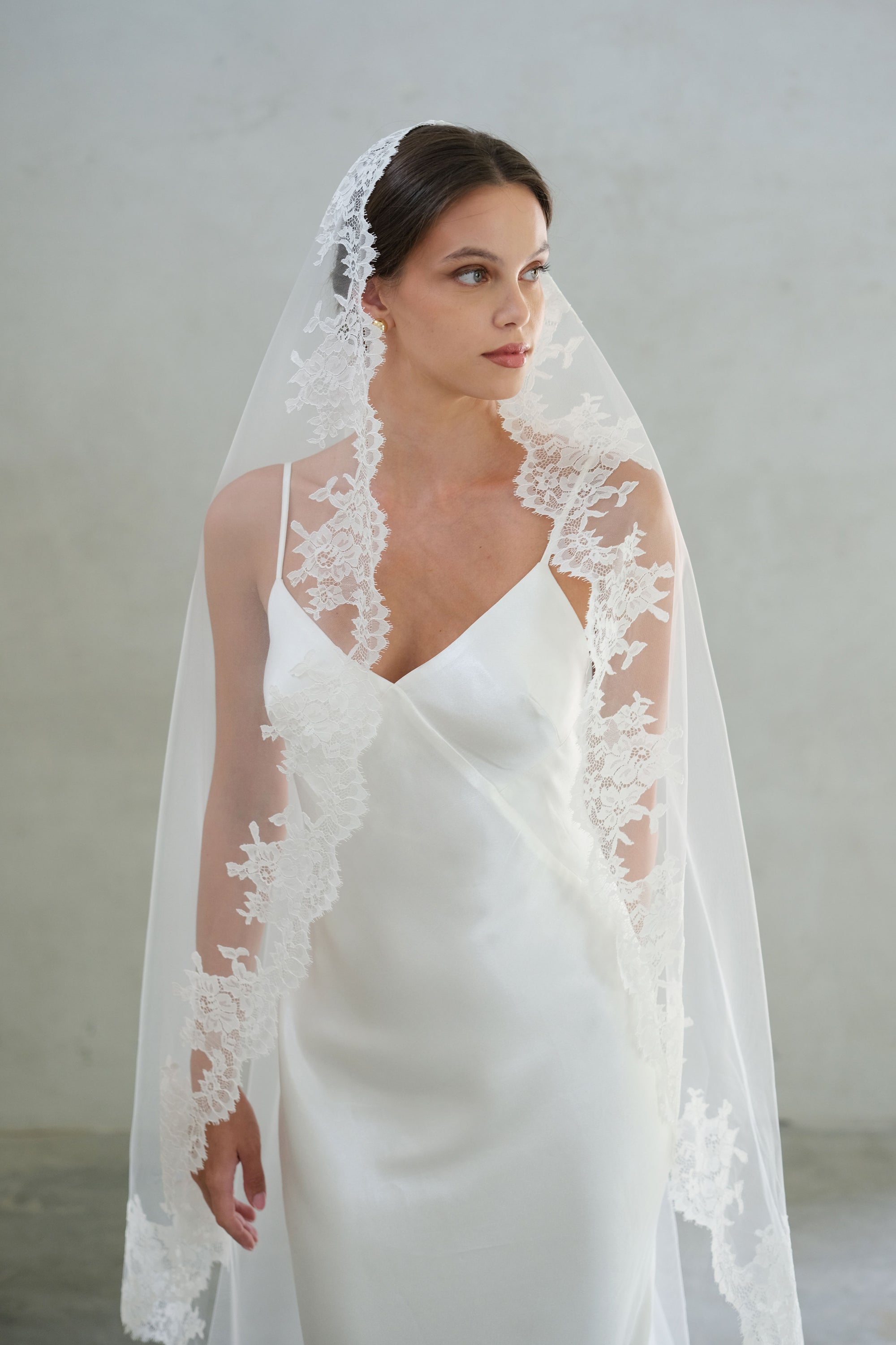 Half length front facing bride wears lace trimmed long mantilla veil