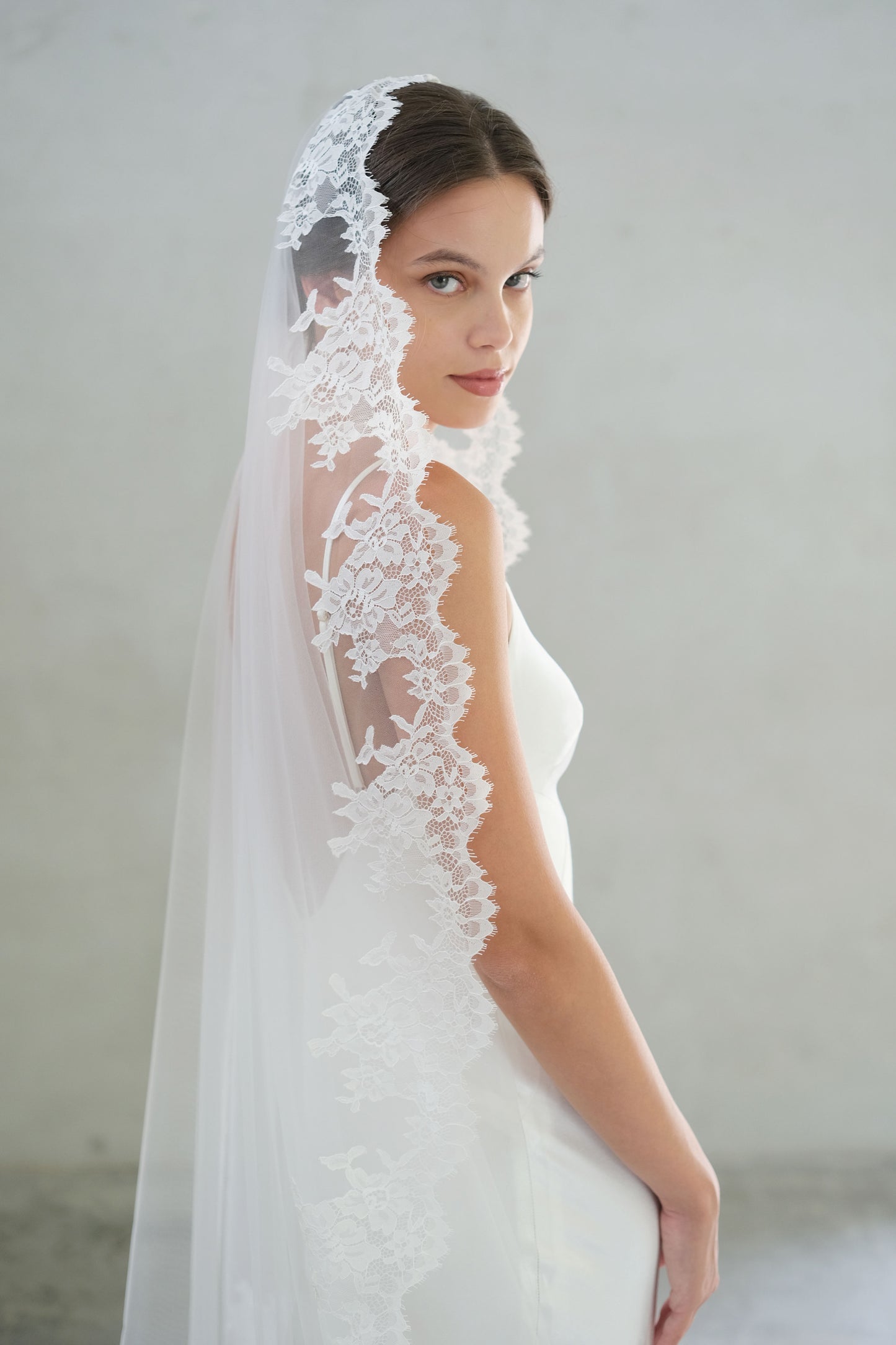 Lace trimmed mantilla veil drapes over the hair and shoulders of bride