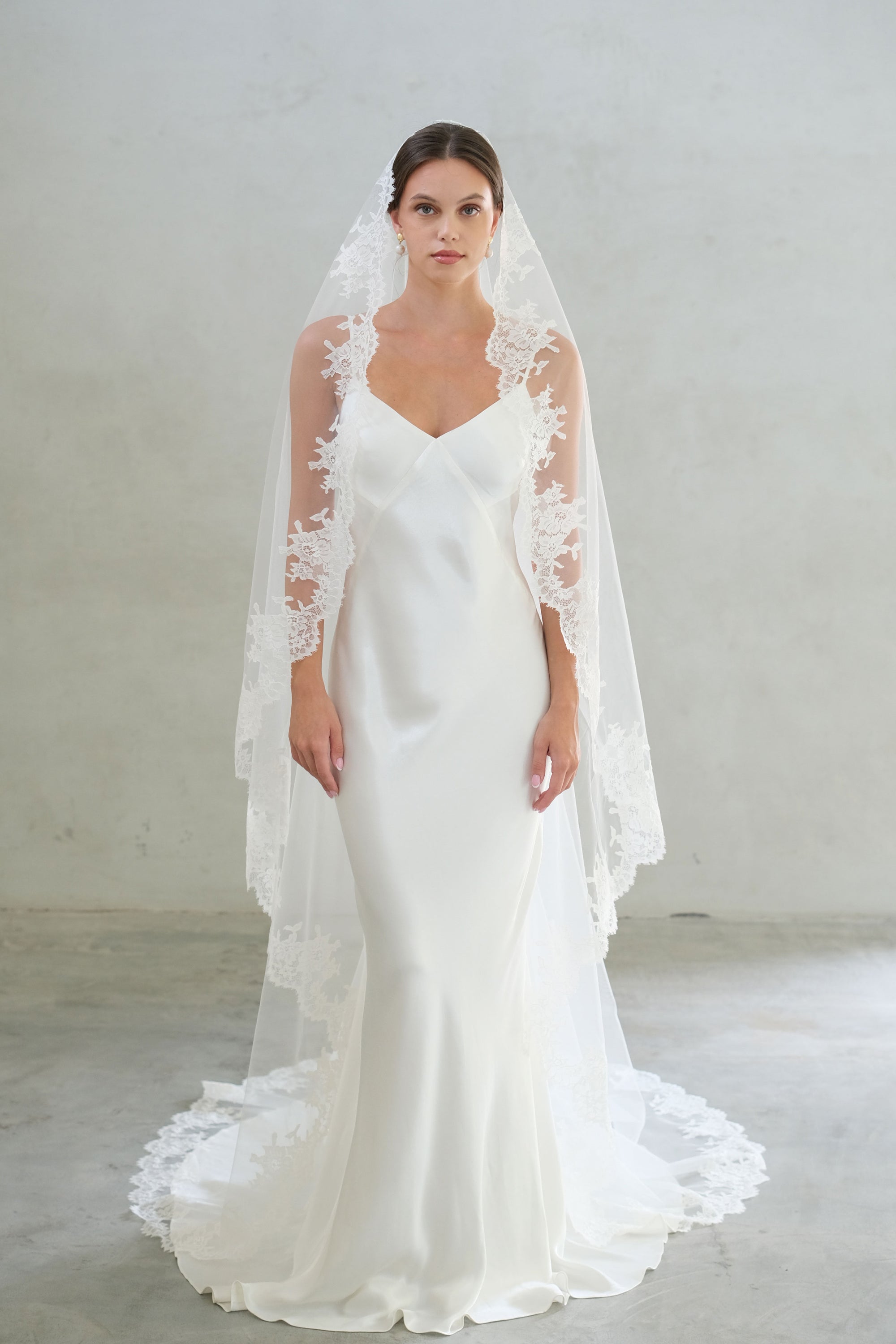 Full length front facing bride wears lace trimmed mantilla veil in chapel length