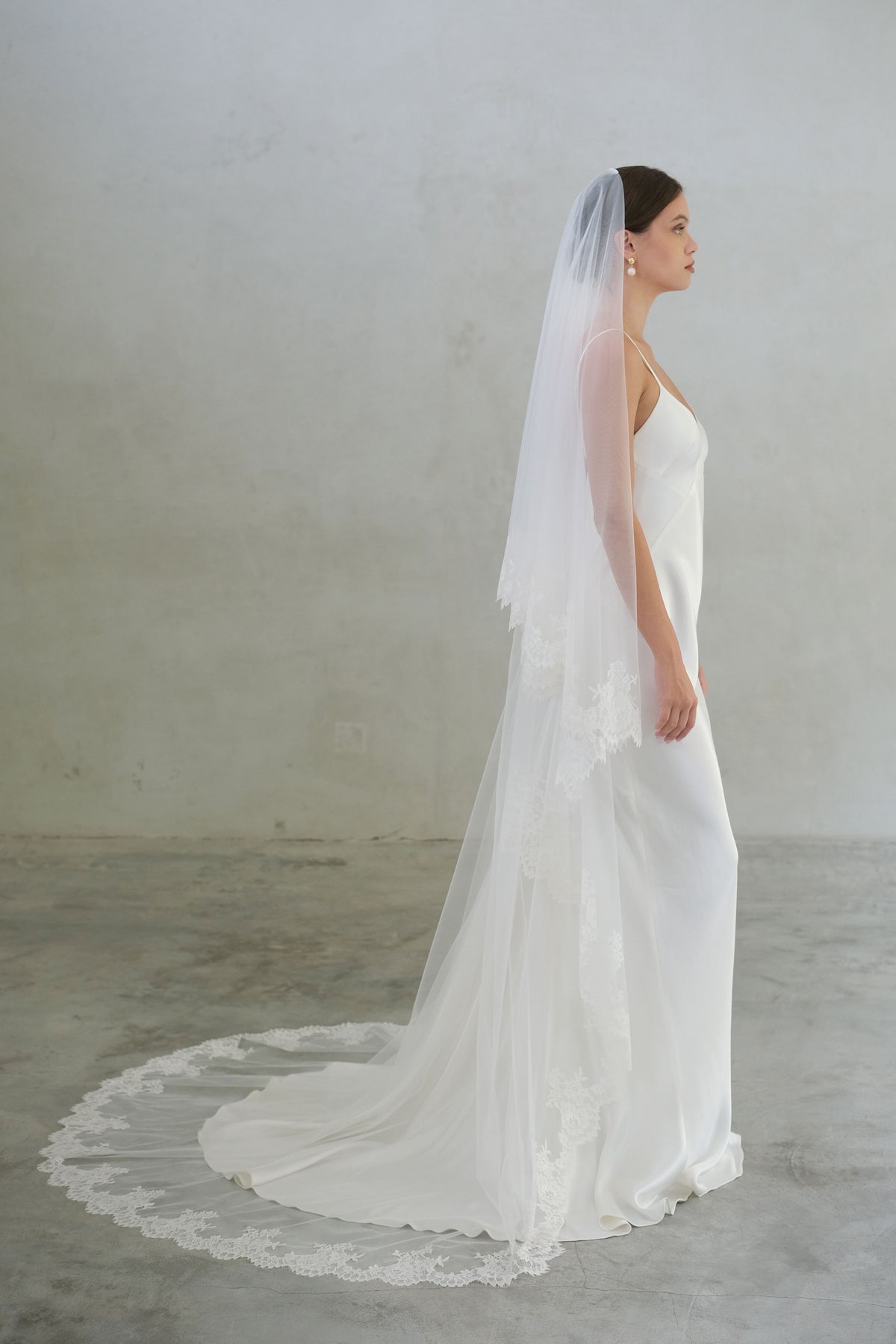 Full length profile of bride wearing long, two tier tulle veil with lace trim showing blusher off 