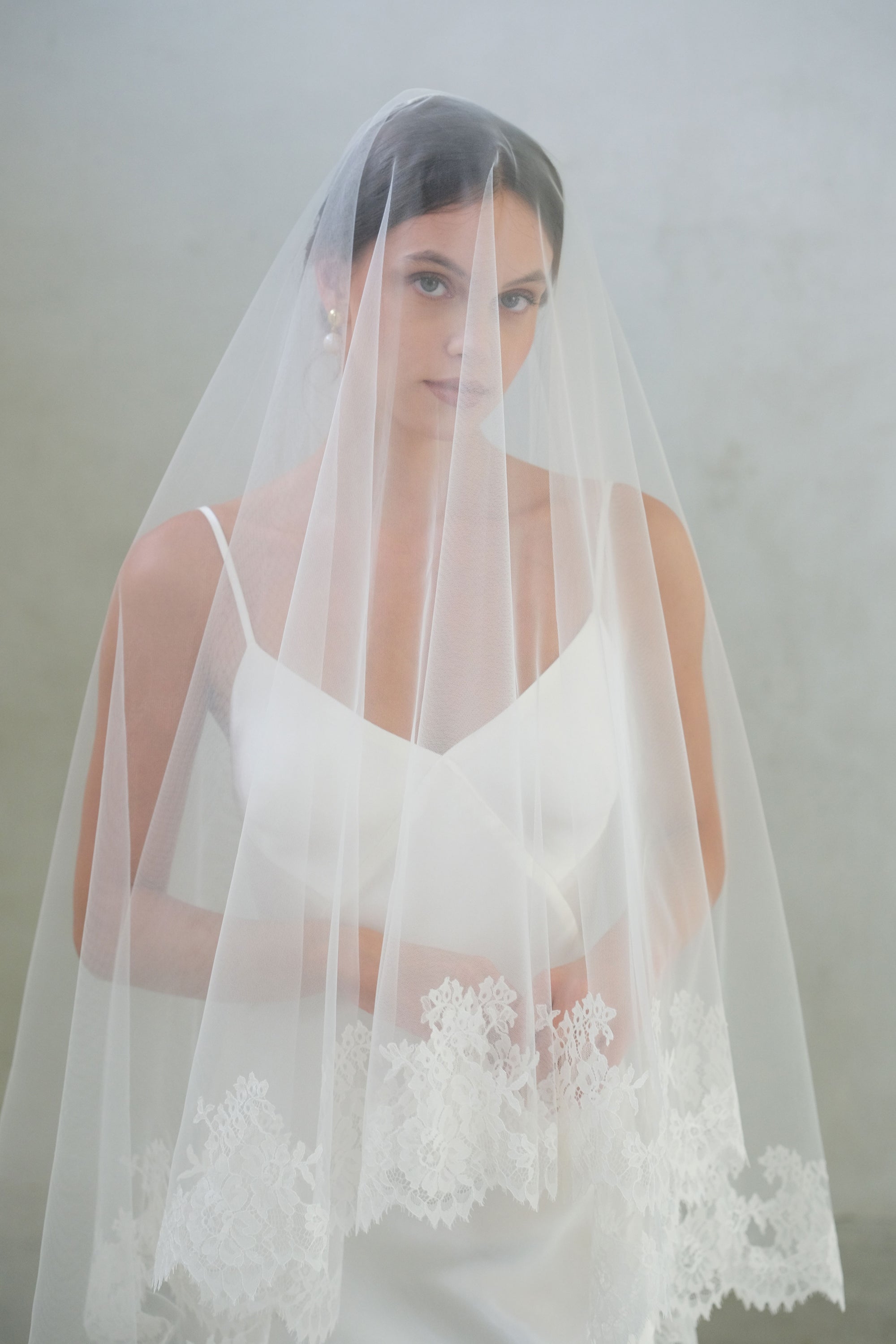 Bride wears long veil shown with blusher down and featuring delicate lace edging