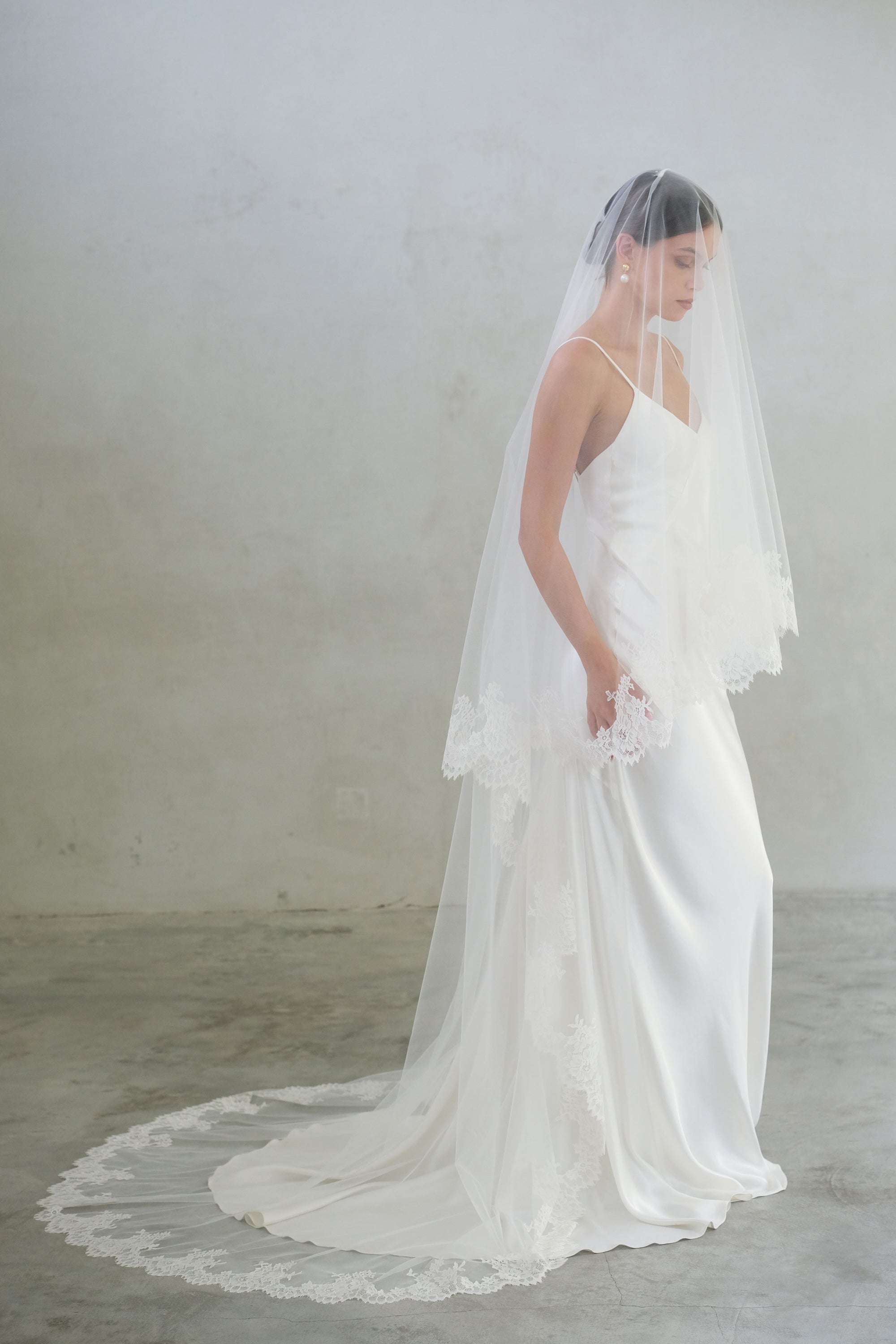 Full length side view of bride wearing long two tier lace edged wedding veil, blusher down