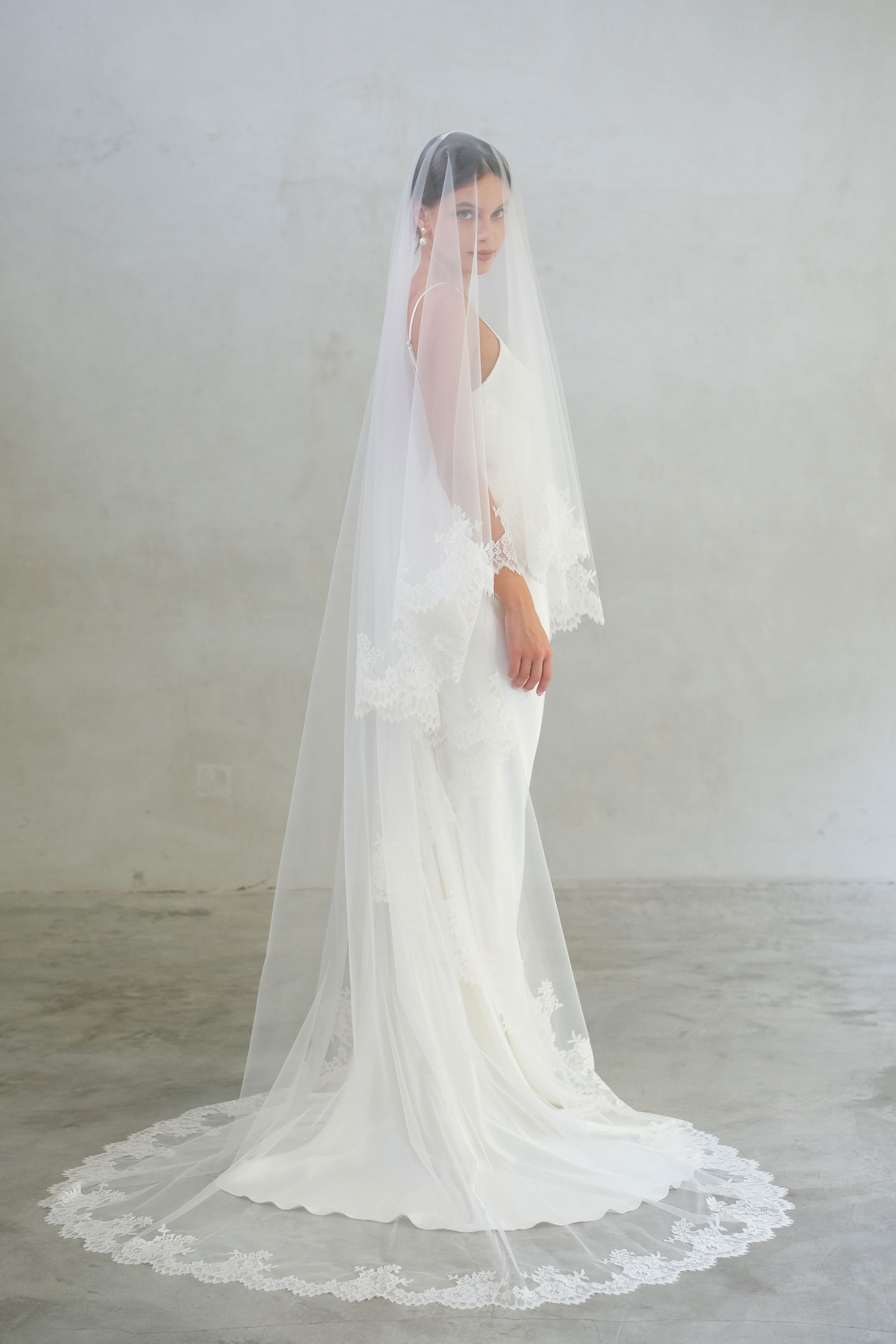 Full length side view of chapel length two tier wedding veil featuring lace edging and blusher down