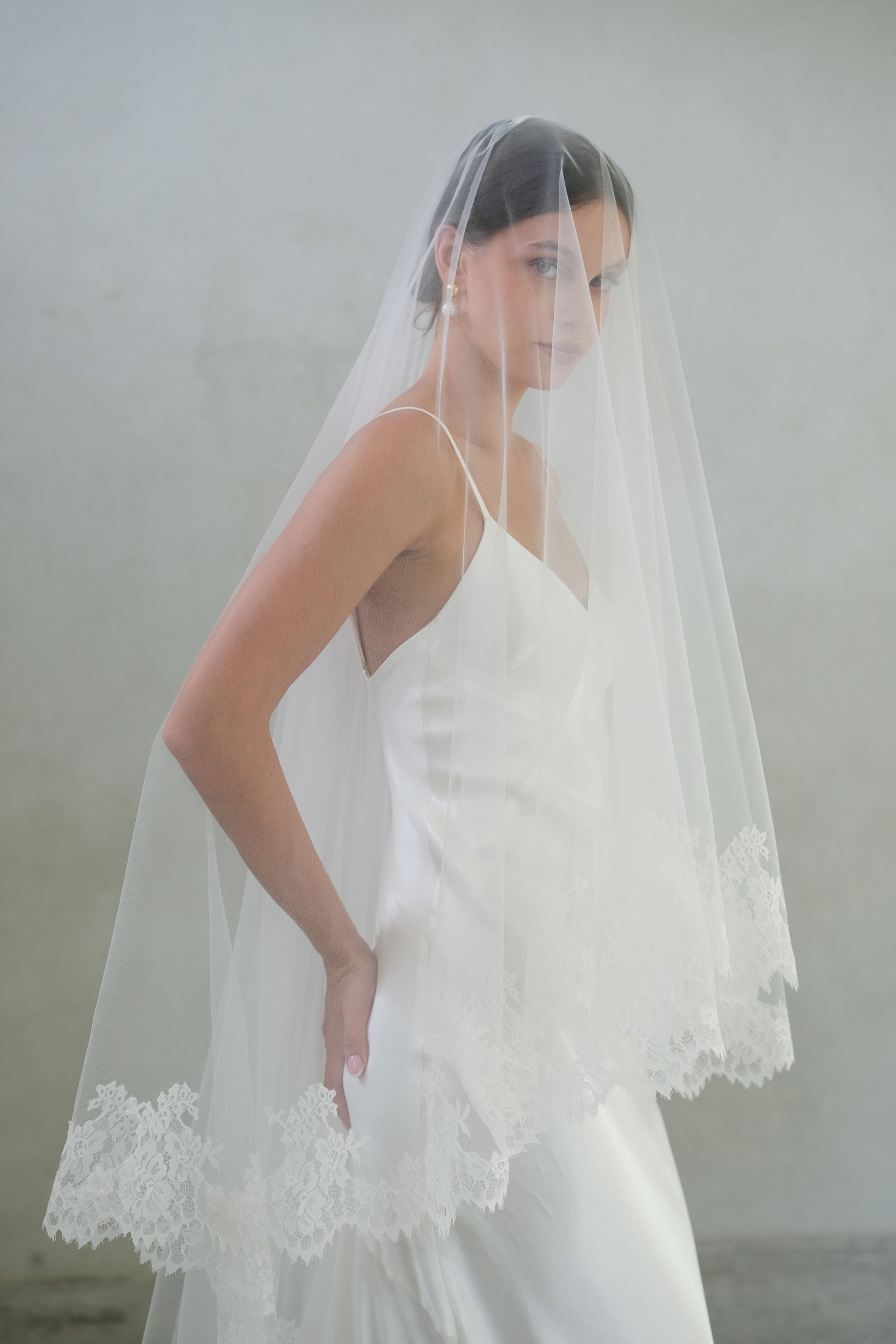 Half length side view of bride wearing blusher down on long lace trimmed wedding veil