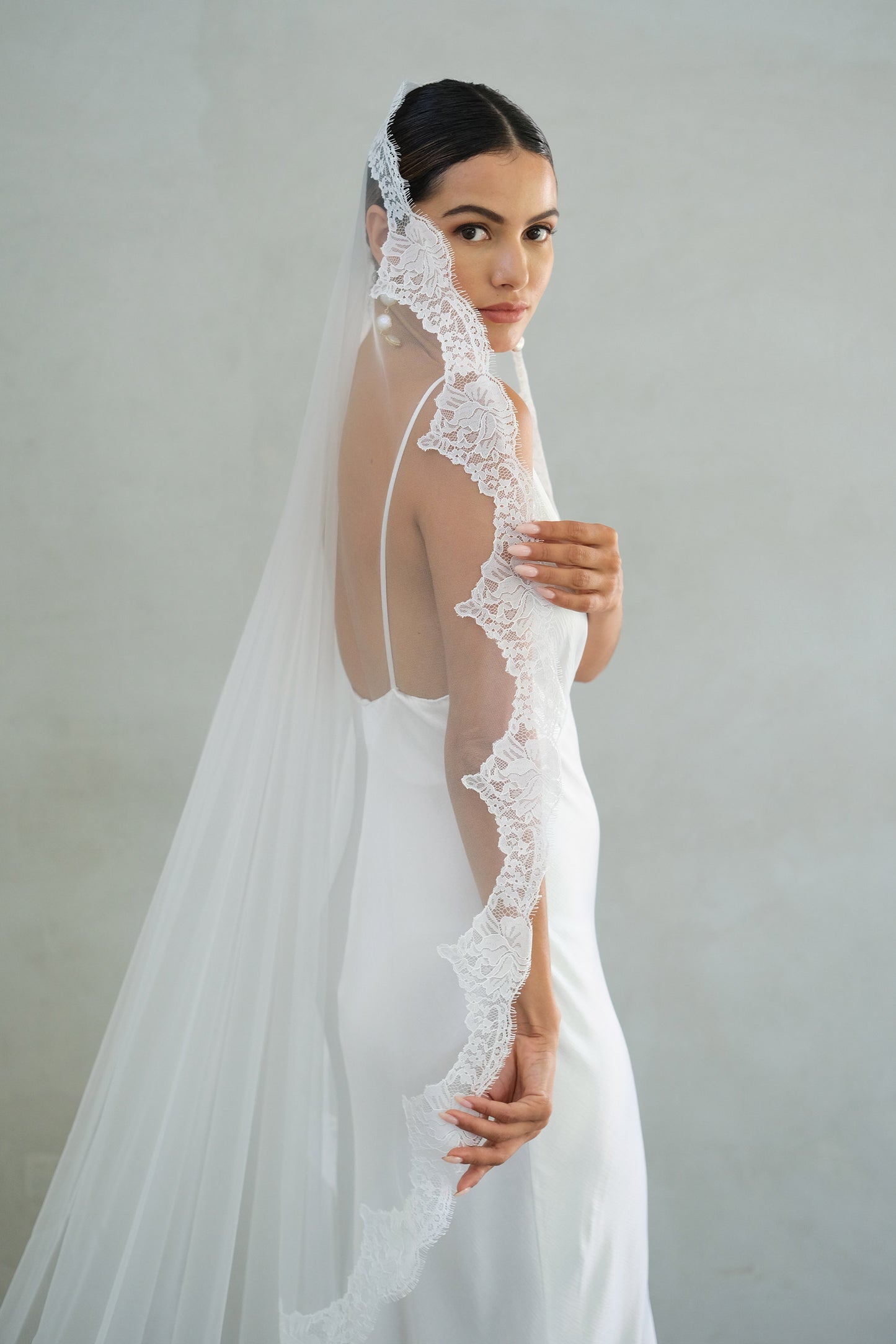 Bride holds lace trim of long mantilla veil