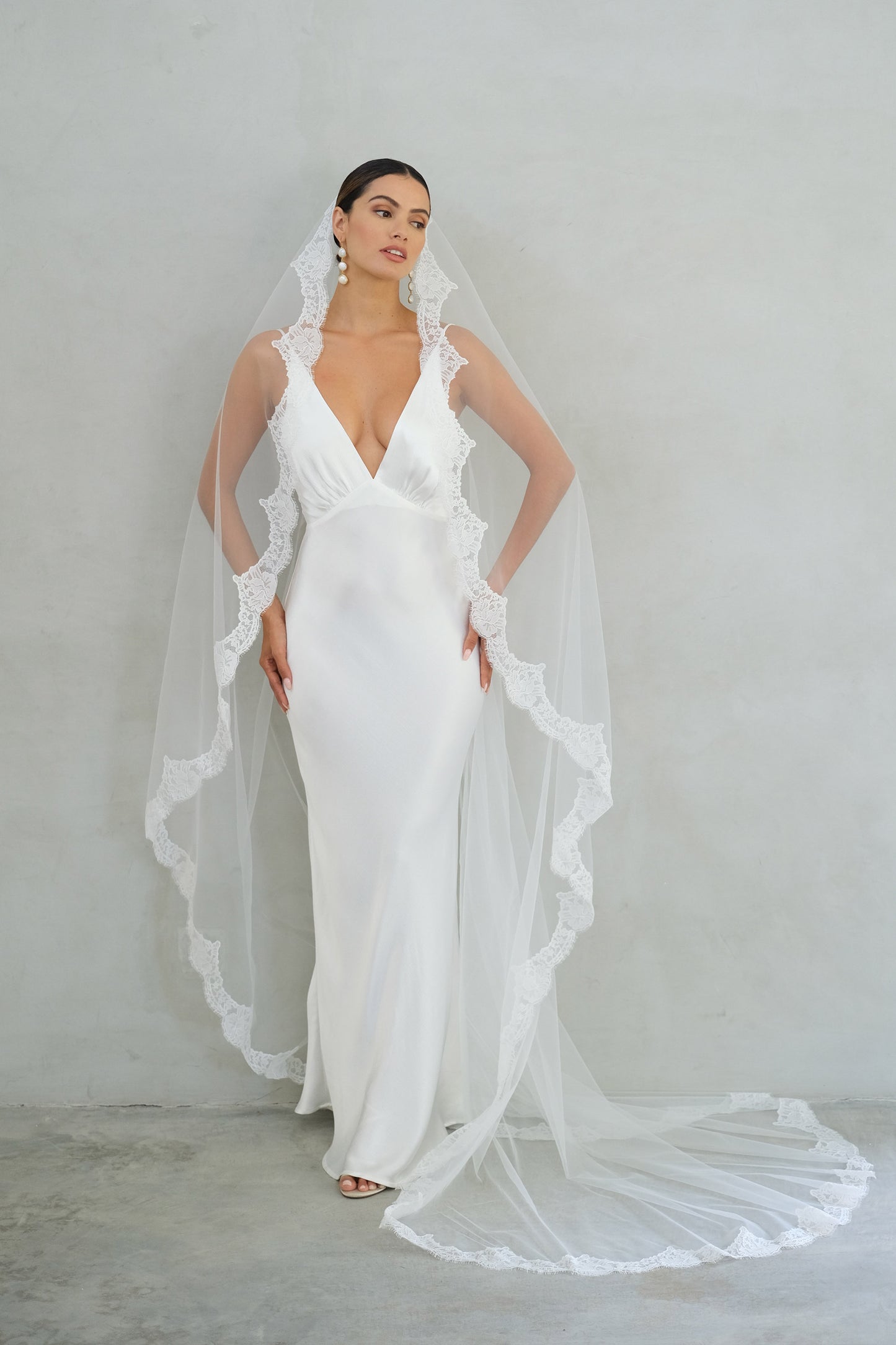 Full length front facing bride wears long mantilla veil trimmed with lace scallops
