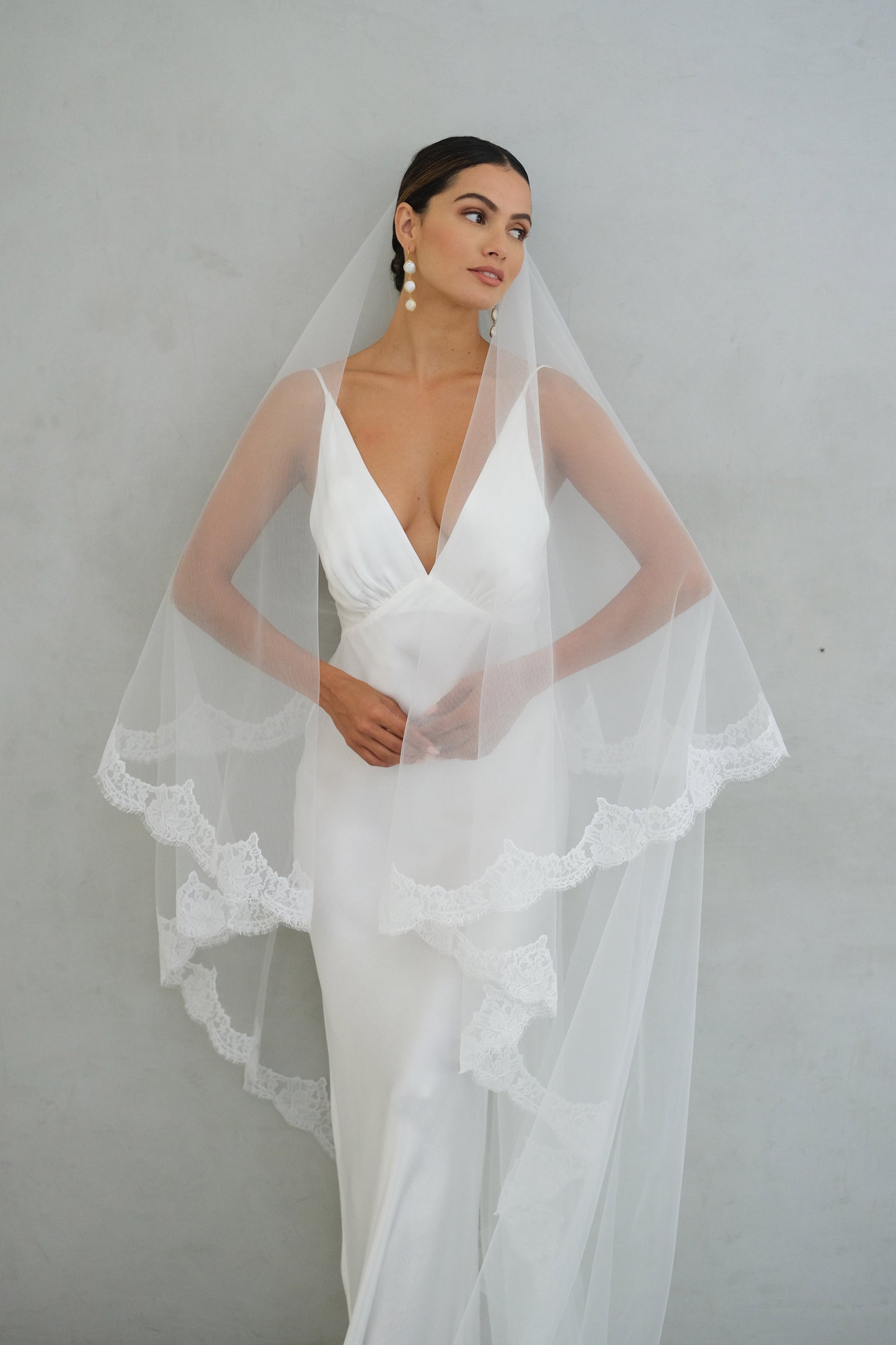 Fron facing bride models lace trimmed wedding veil shown with bllusher off