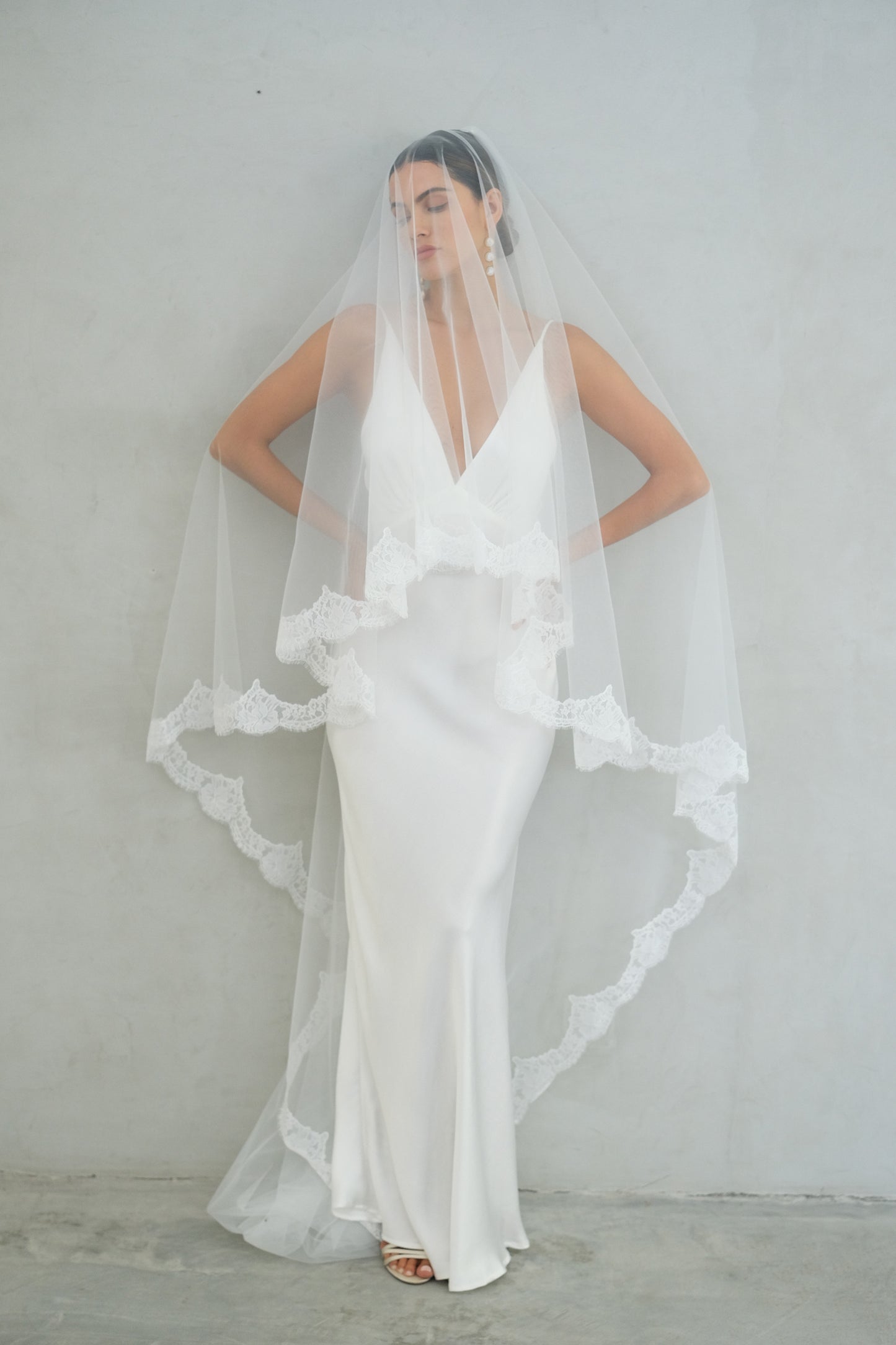 Full length front facing bride models long two tier wedding veil with lace trim; blusher down
