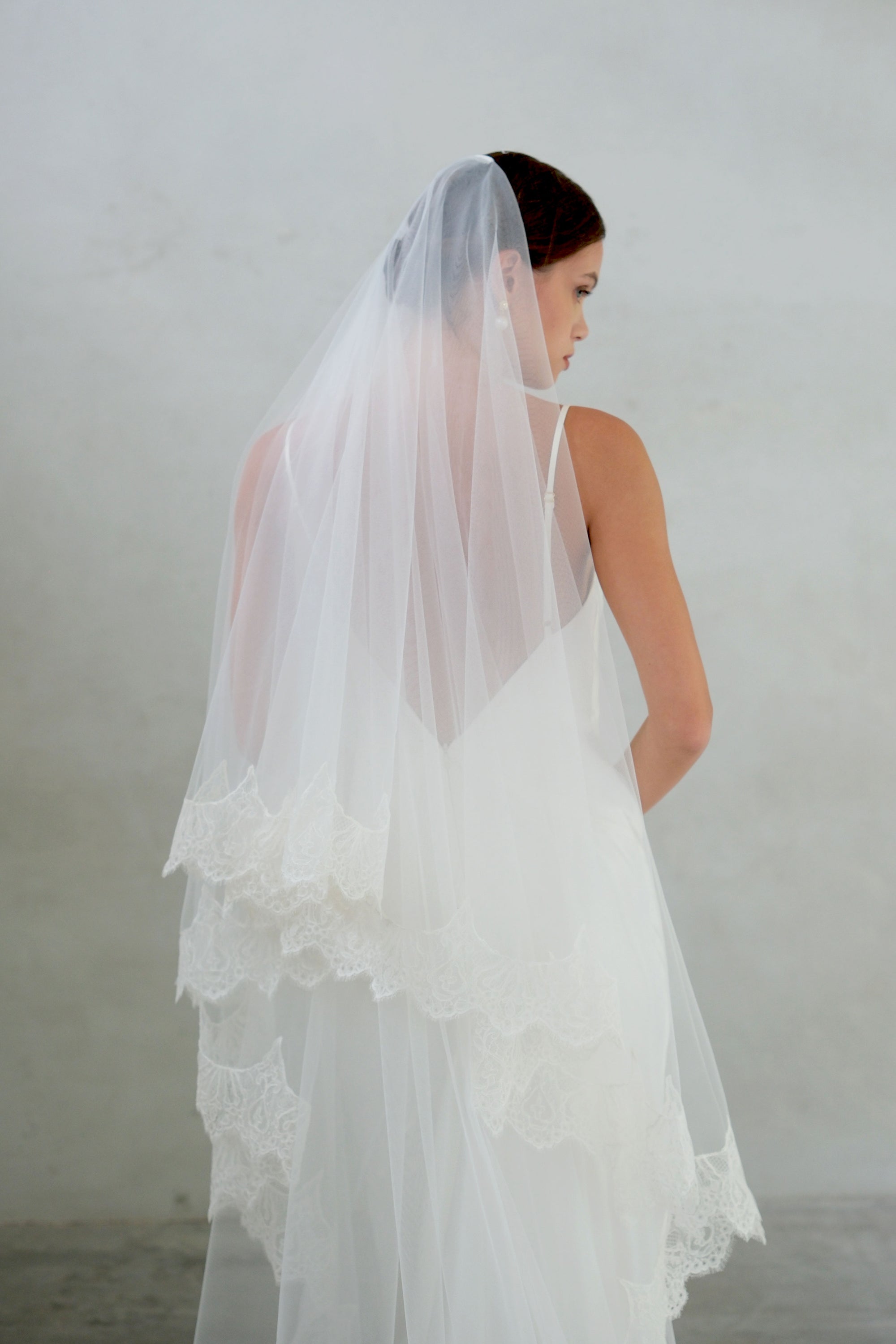 Back view of bride in profile wearing lace trimmed veil with blusher off