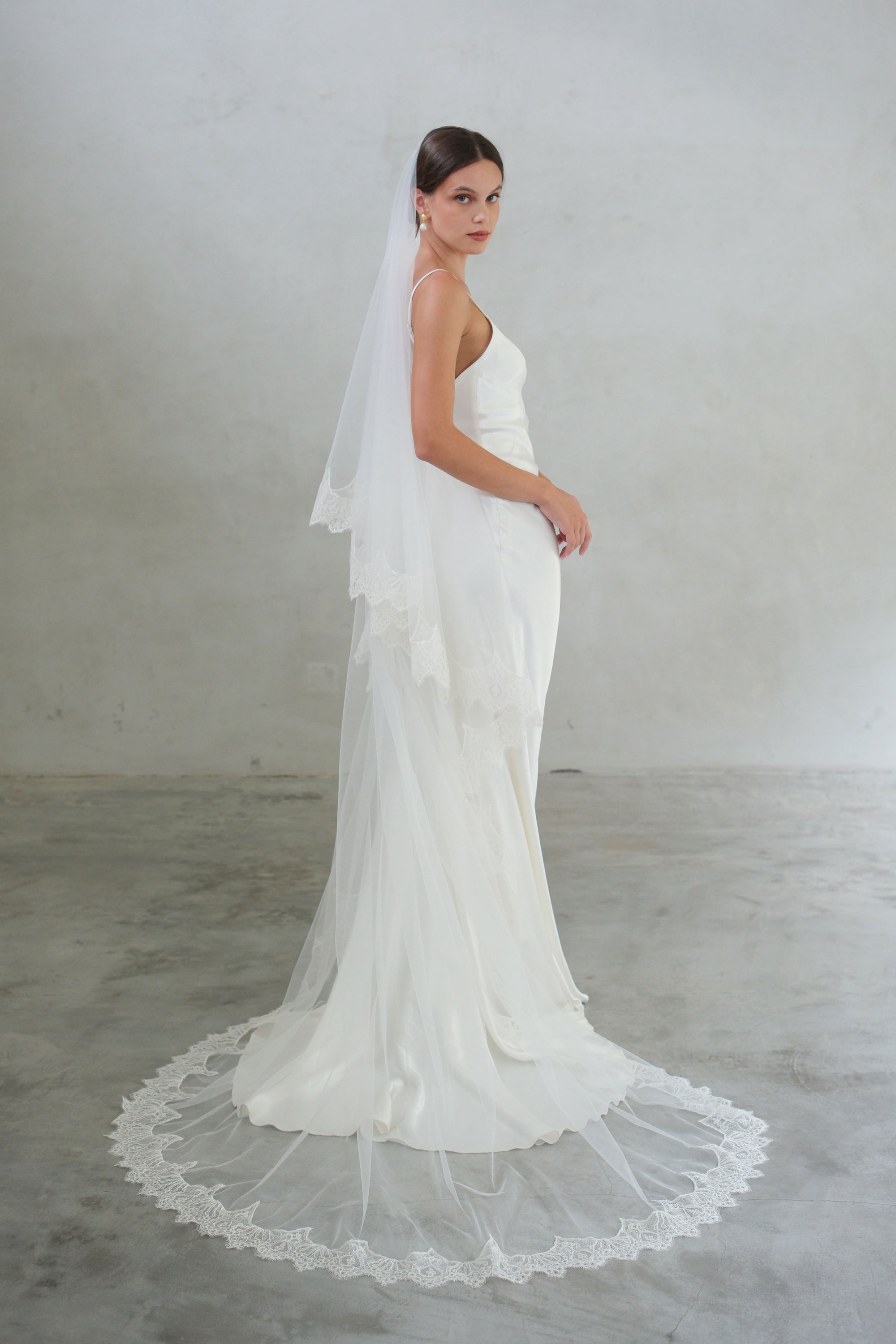 Bride turns to show long two tier wedding veil with delicate lace trim; blusher off