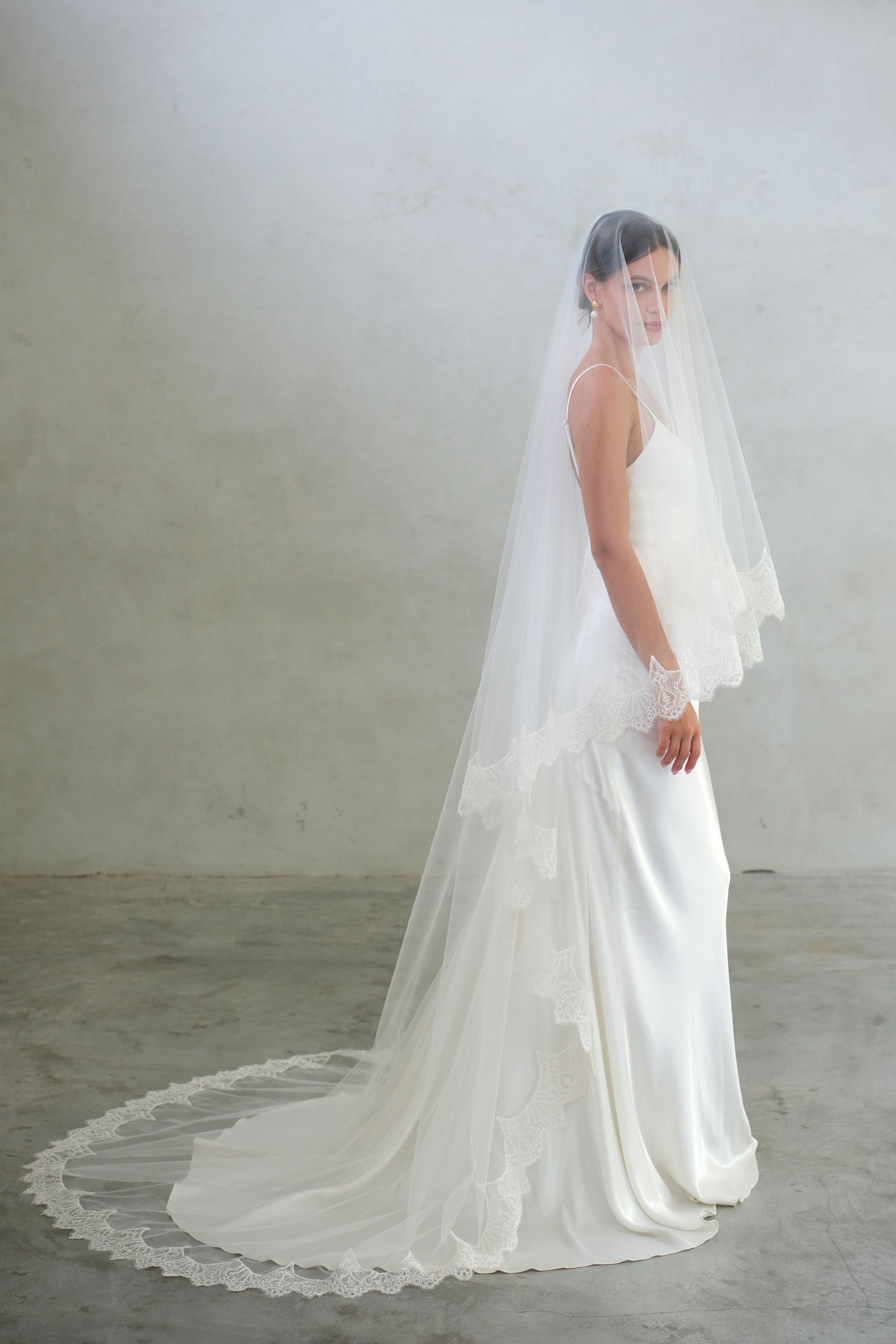 Full length side view showing bride wearing two tier, lace edged veil in chapel length and ivory colour