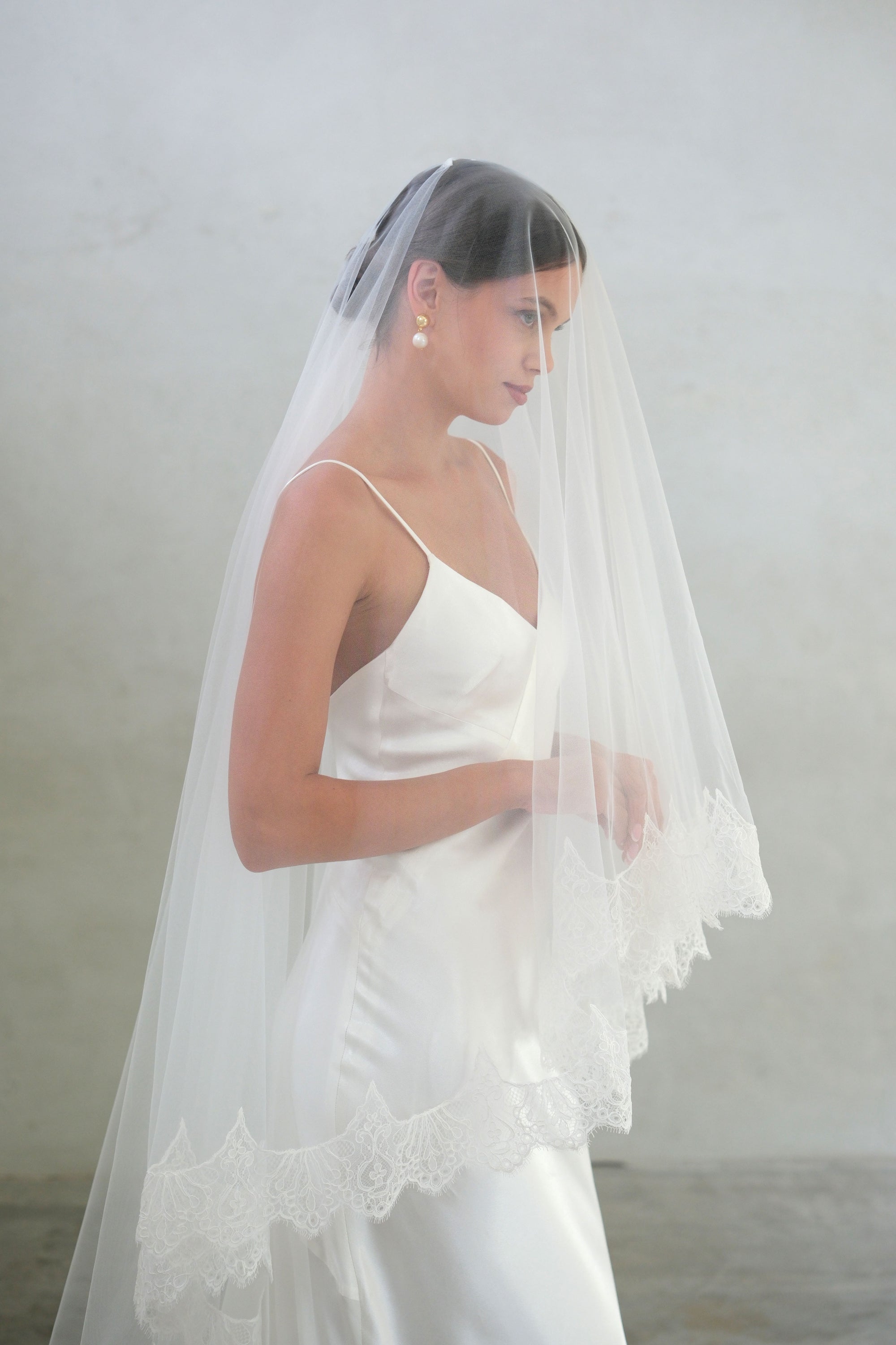 Half length profile showing bride with blusher down on long laced edged veil