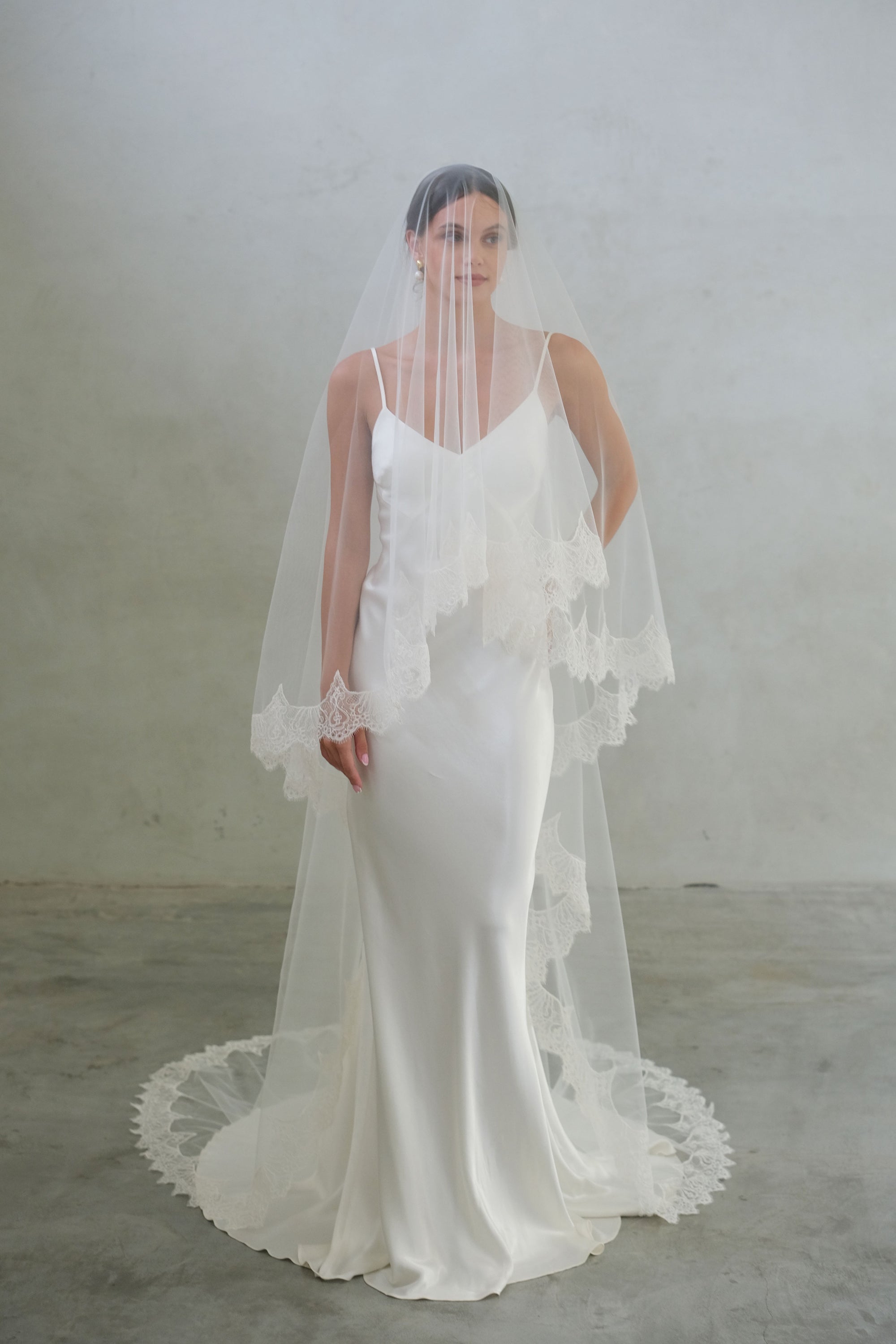 Full length front facing bride wears two tier, long laced edged veil in ivory colour with lace edging