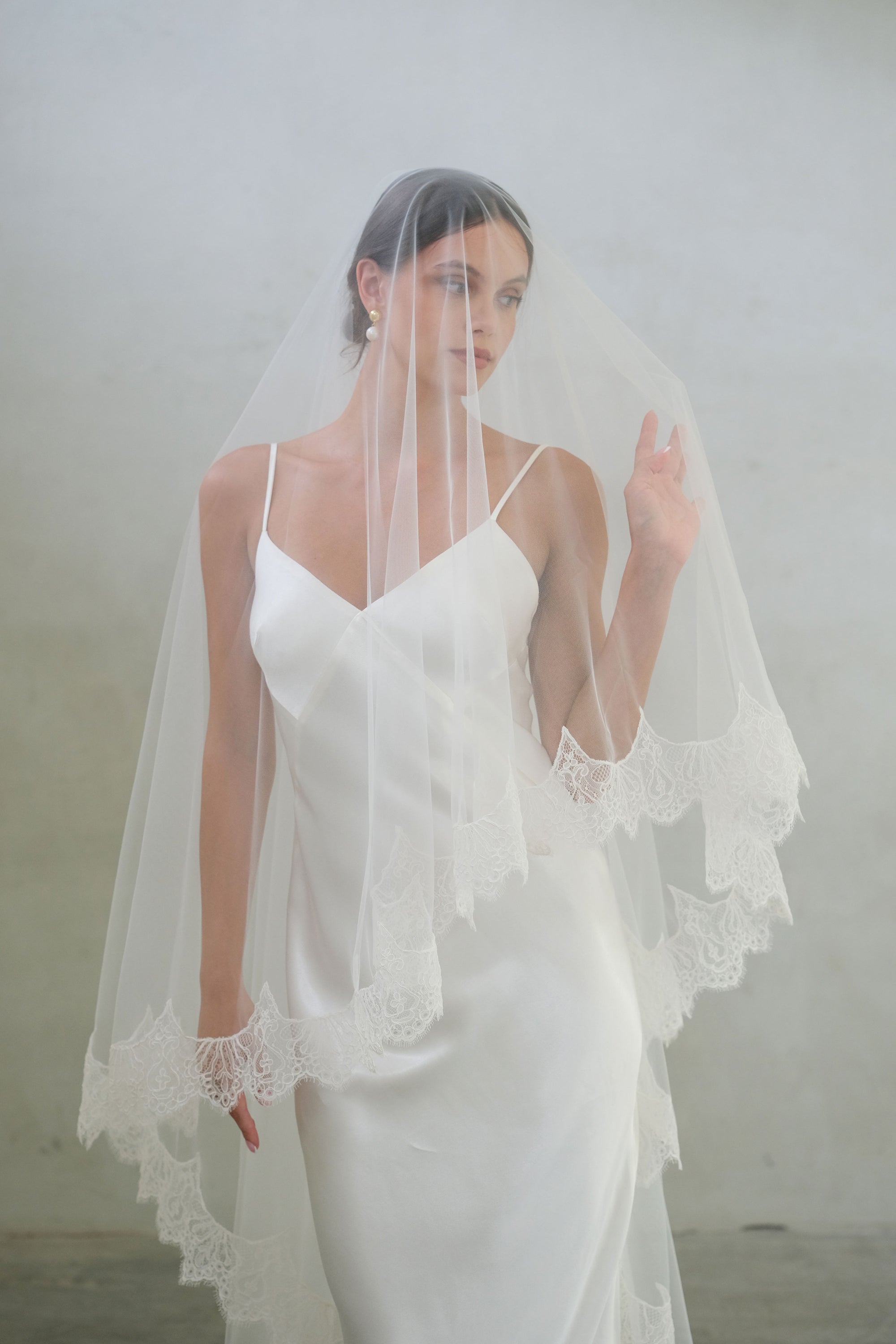 Half length front facing bride wears long veil with blusher and delicate lace trim