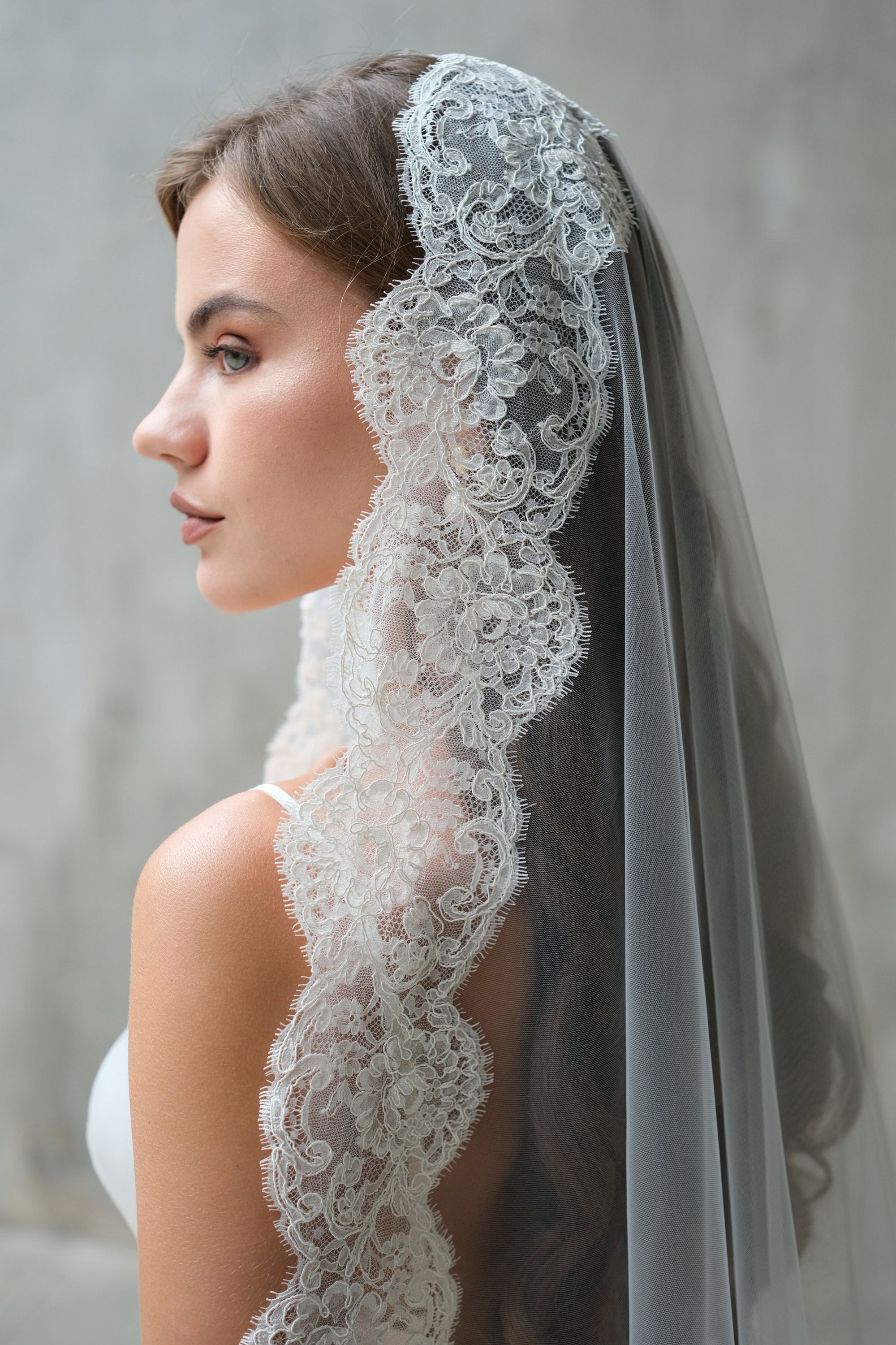 Close-up shows detail of floral lace trim on mantilla veil worn by bride in profile