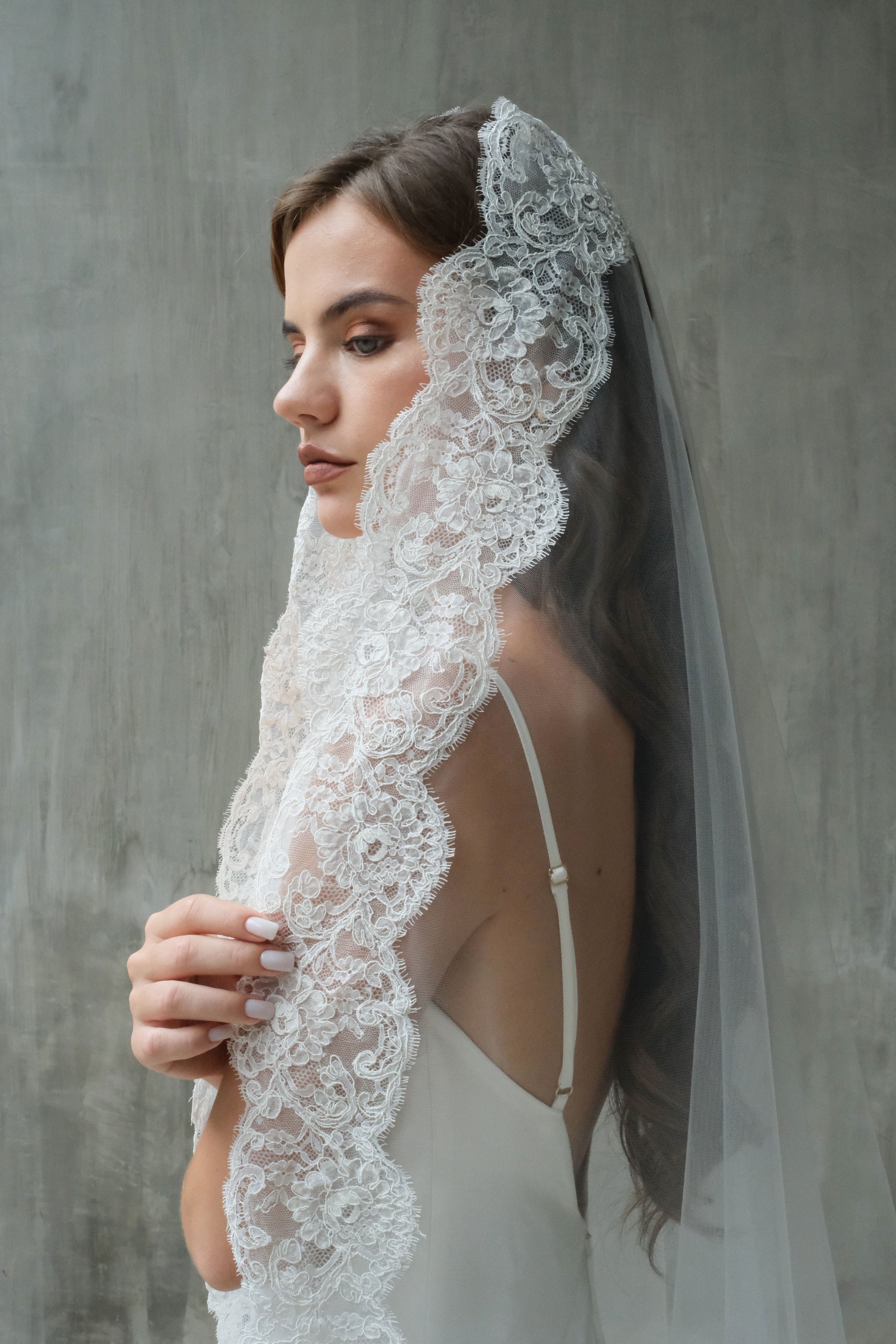 Bride in profile wears lace edged mantilla veil over hair and shoulders