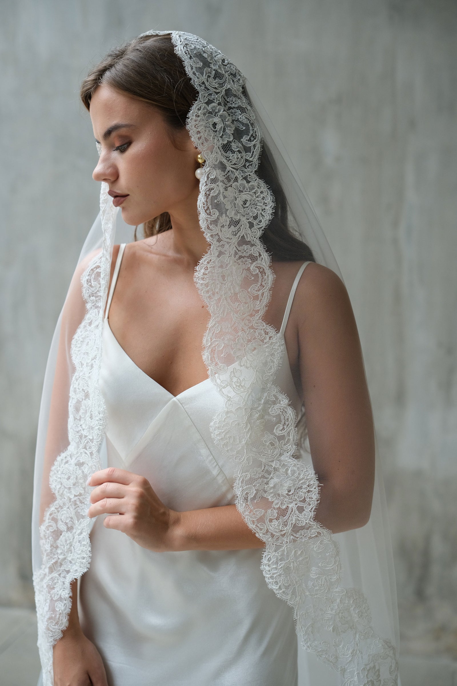 Corded lace trim of mantilla bridal veil drapes over bride's head and shoulders