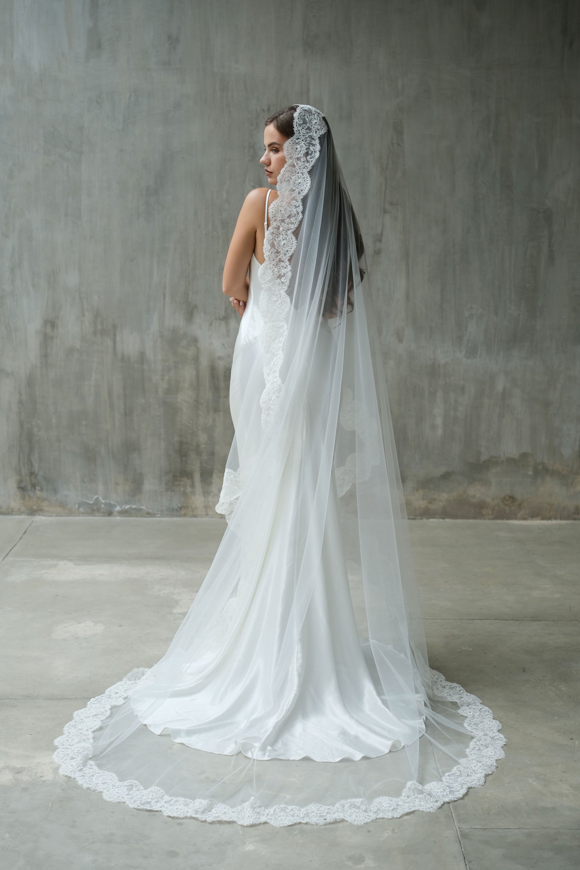 Full length back view of bride turning to show lace trim of one-tiered chapel length bridal veil