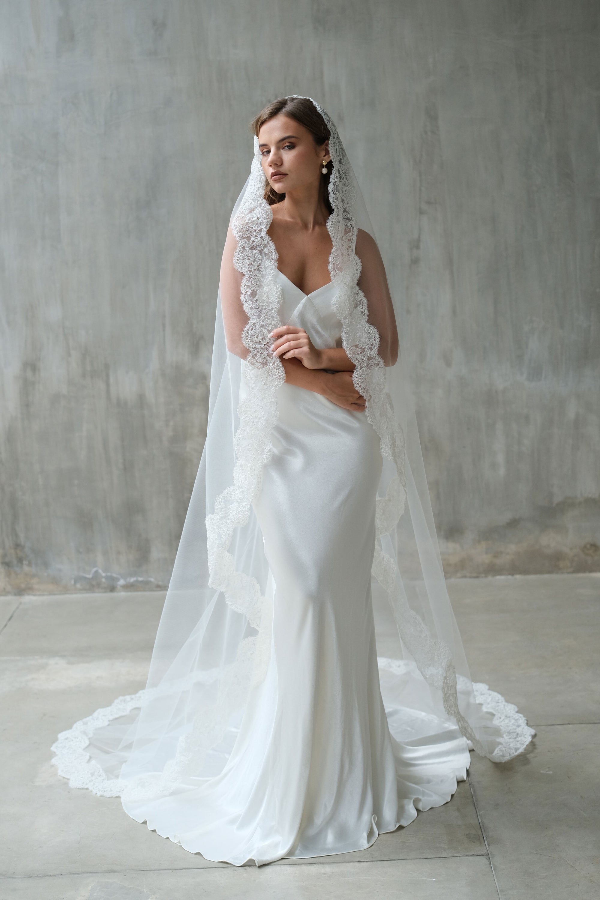 Full length front facing bride wears long mantilla veil trimmed with corded floral lace