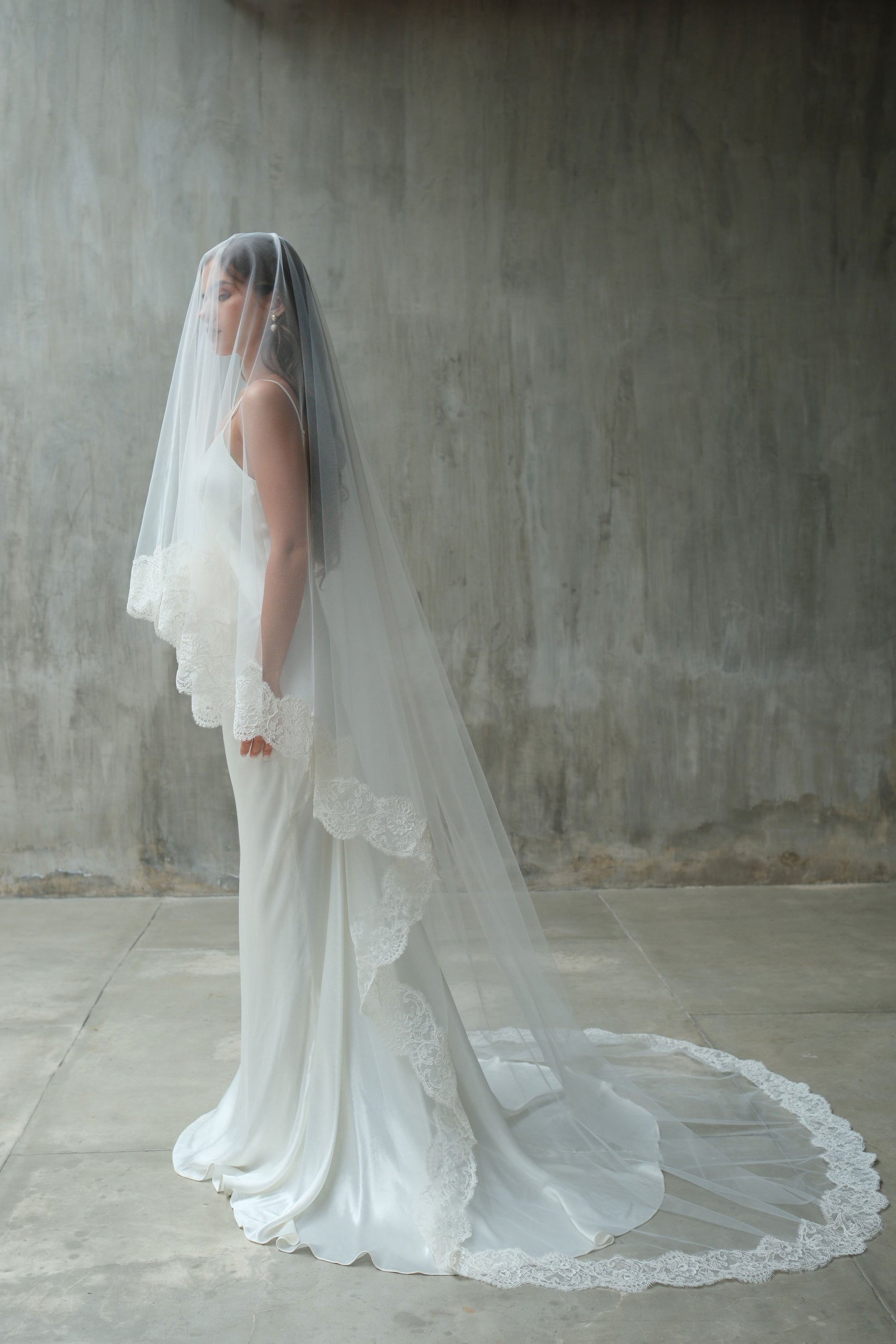 Full length side view showing long lace edged wedding veil with blusher down