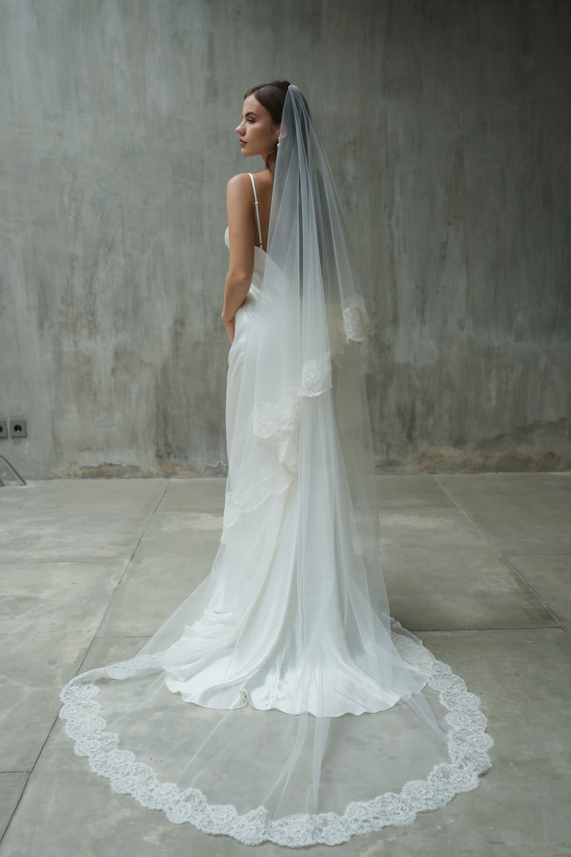 Full length shot of bride wearing long, two tier wedding veil with blusher off and elaborate lace edging