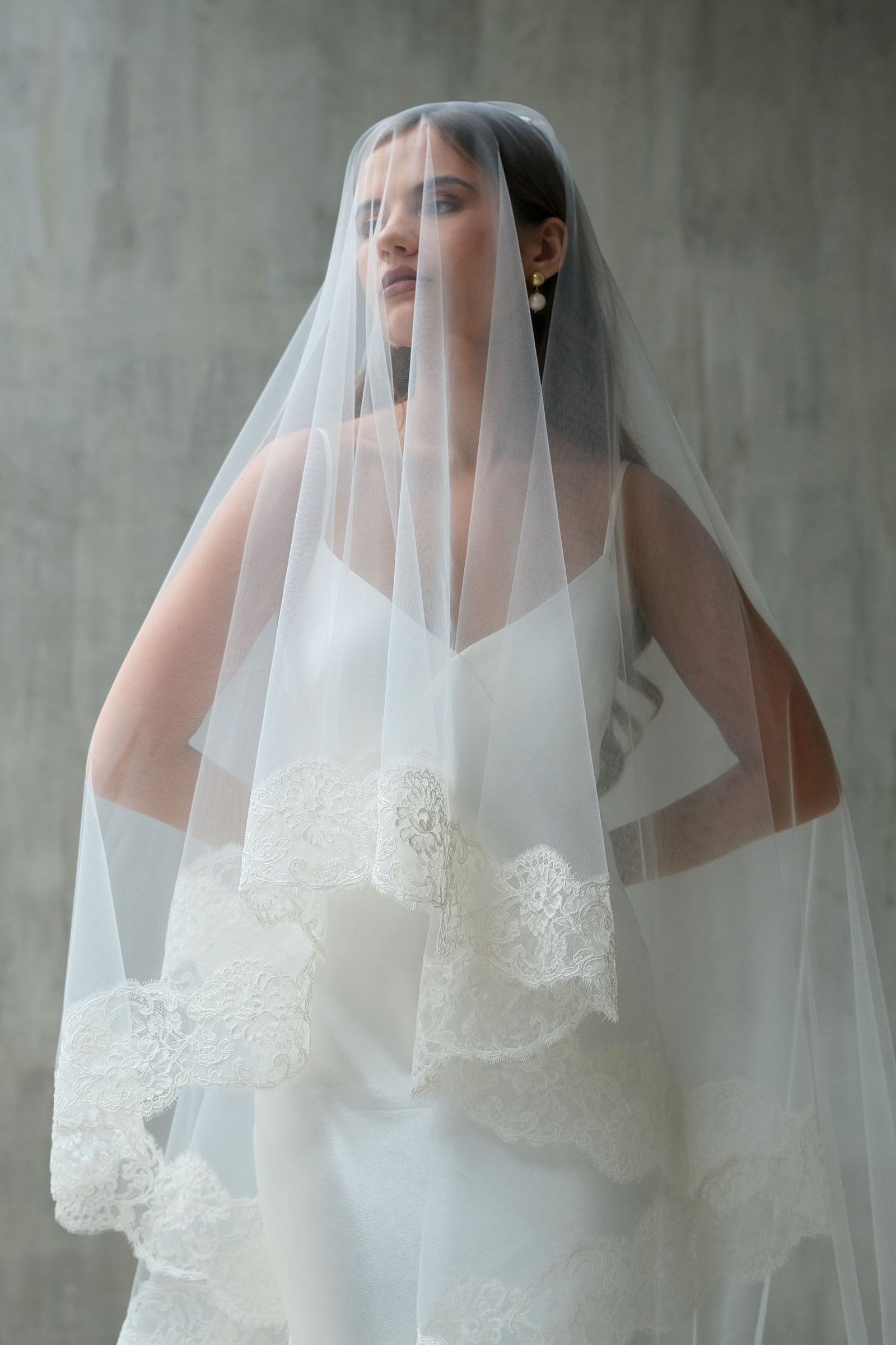 Half length front facing bride wears two tier laced edge wedding veil, blusher down