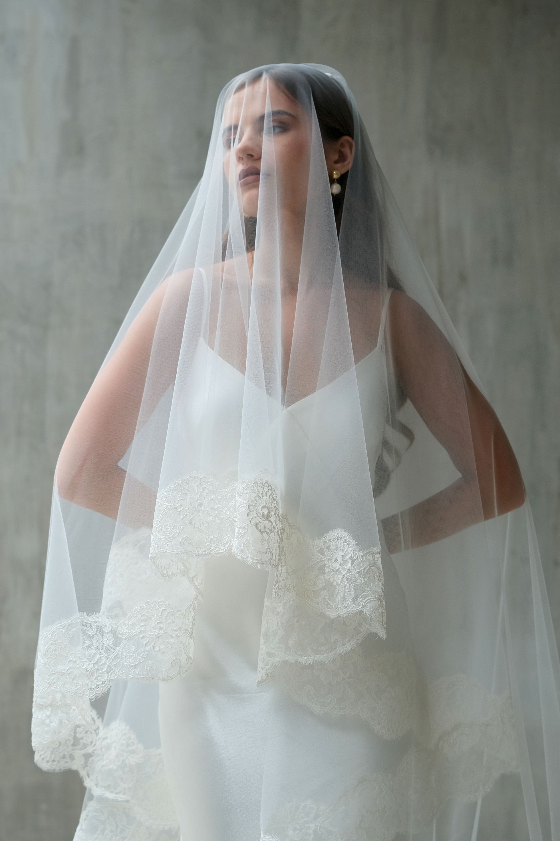 Half length front facing bride wears two tier laced edge wedding veil, blusher down