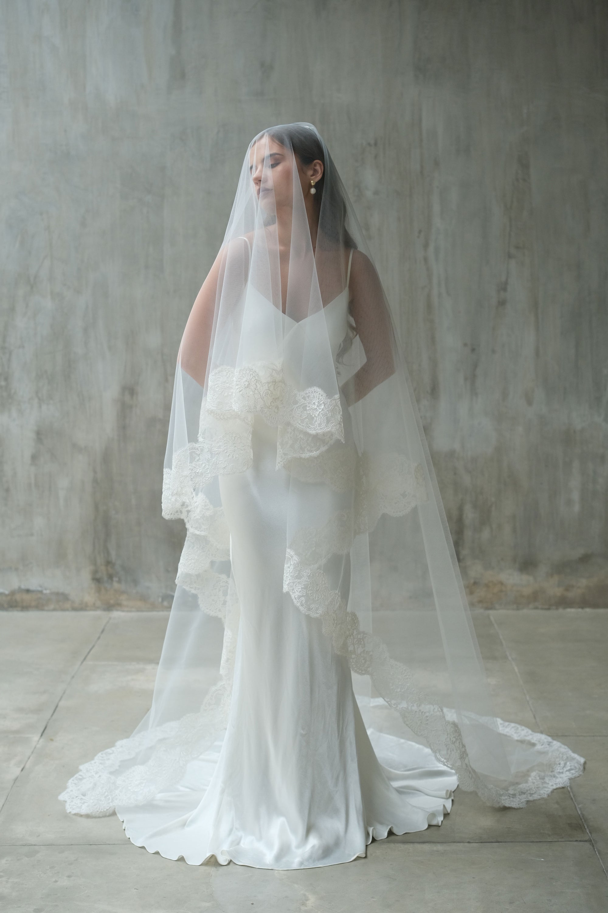 Full length front facing bride wears long drop veil featuring elaborate corded lace trim