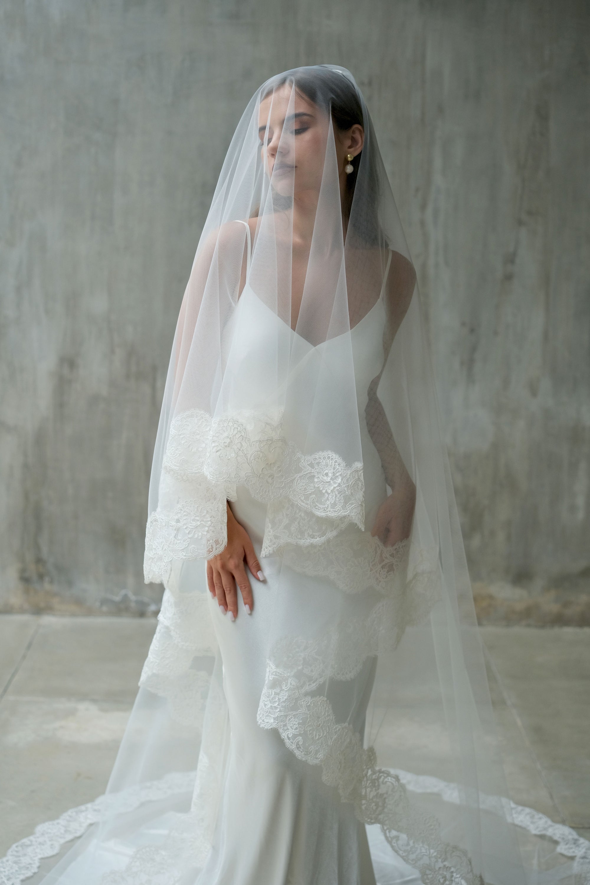 Front facing bride wears long, lace edged wedding veil showing blusher down