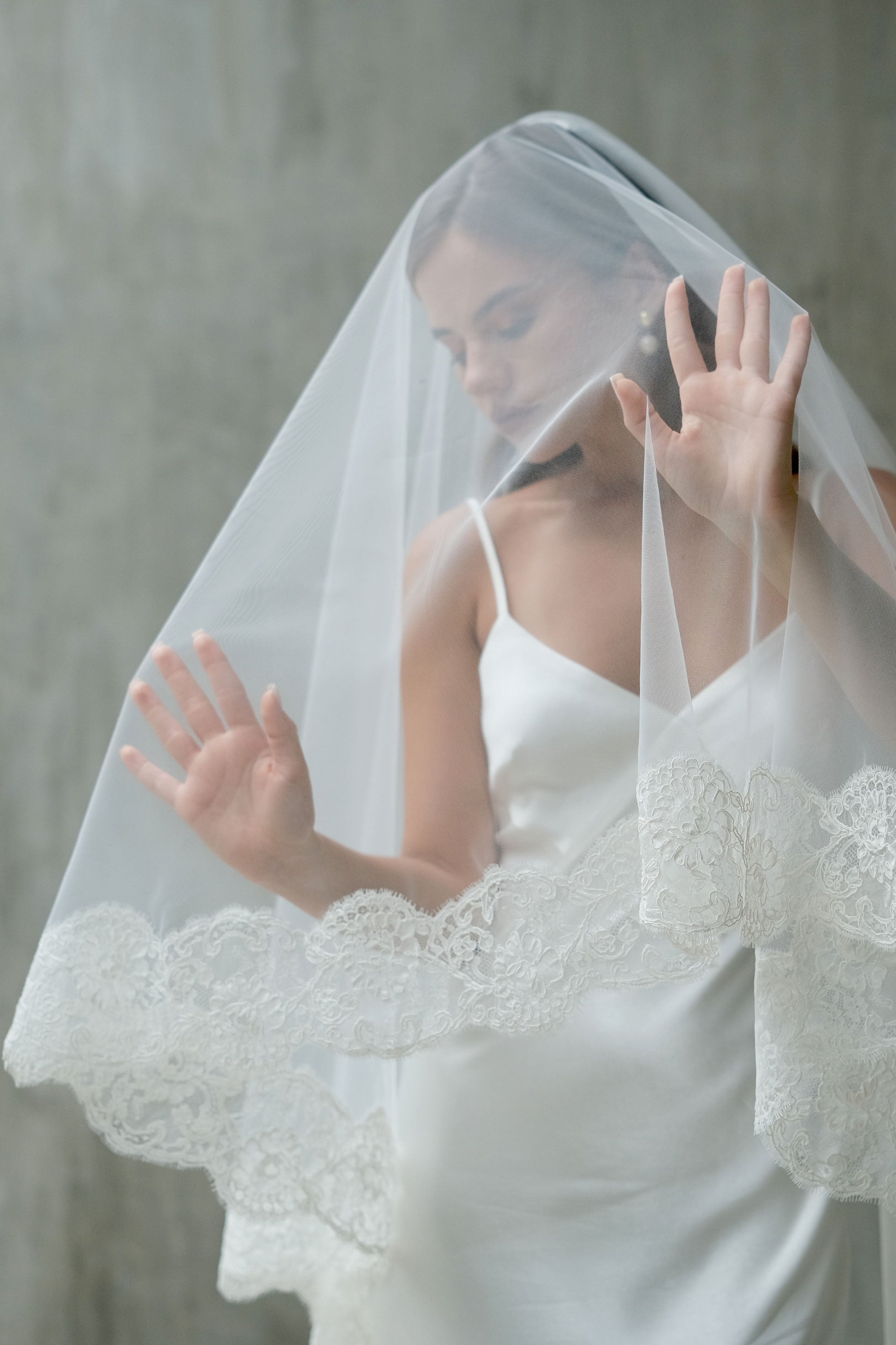 Bride holds up blusher of two tier veil to highlight elaborate corded lace trim