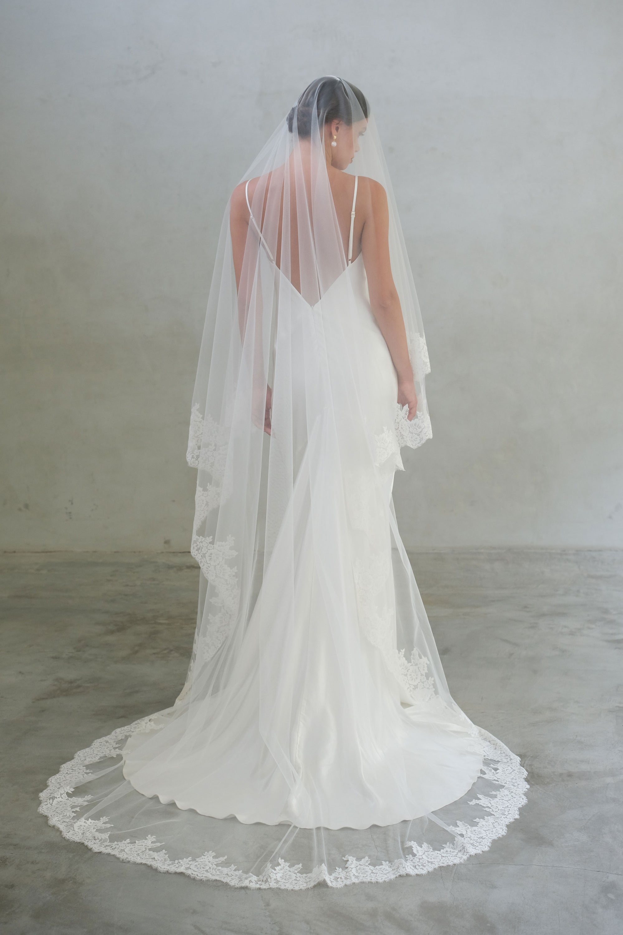 Full length back view of bride wearing chapel length lace trimmed two tier veil; blusher down