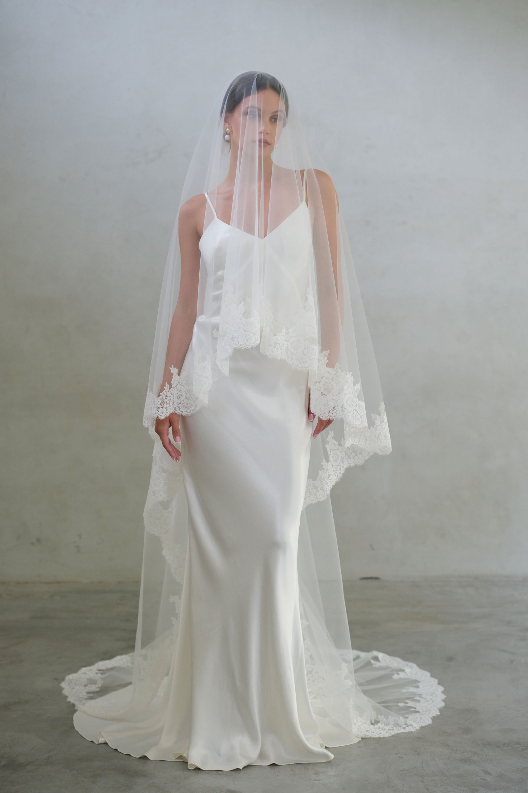 Full length front facing bride wears long, lace trimmed veil showing blusher down