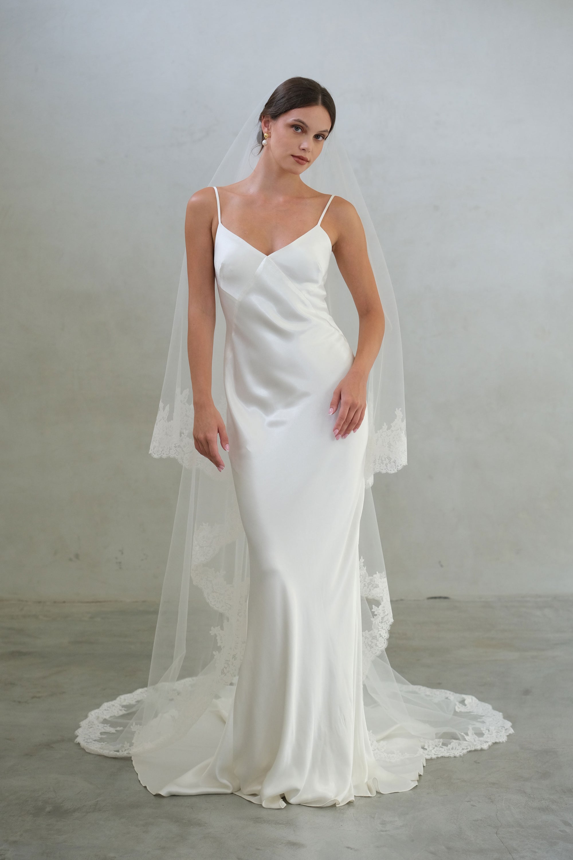 Full length front facing bride wears long, two tier lace edged veil shown with blusher off