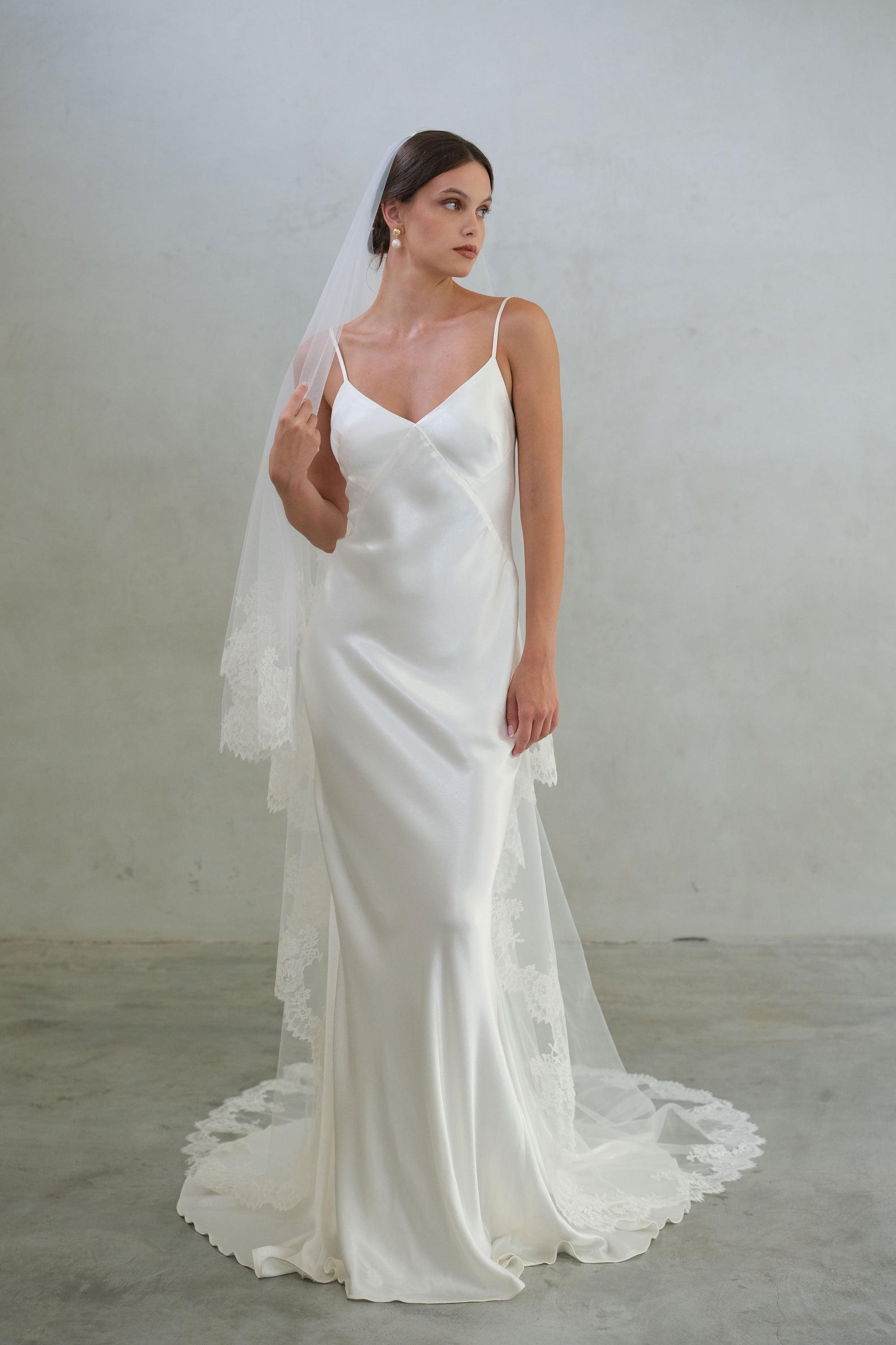 Full length front facing bride wears long, lace edged two tier veil shown with blusher to the back