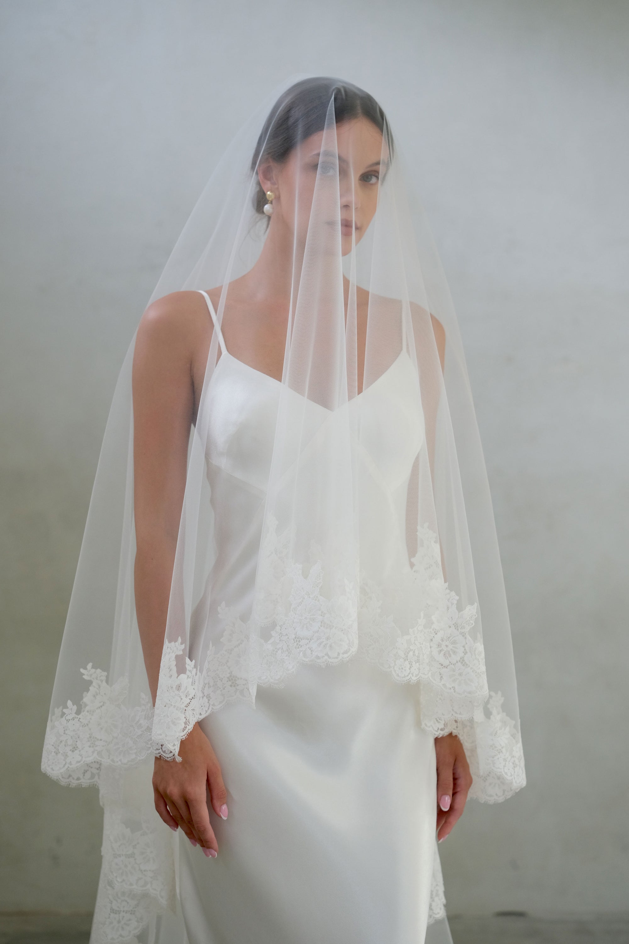 Half length front facing bride wears blusher down on two tier wedding veil with soft lace edging