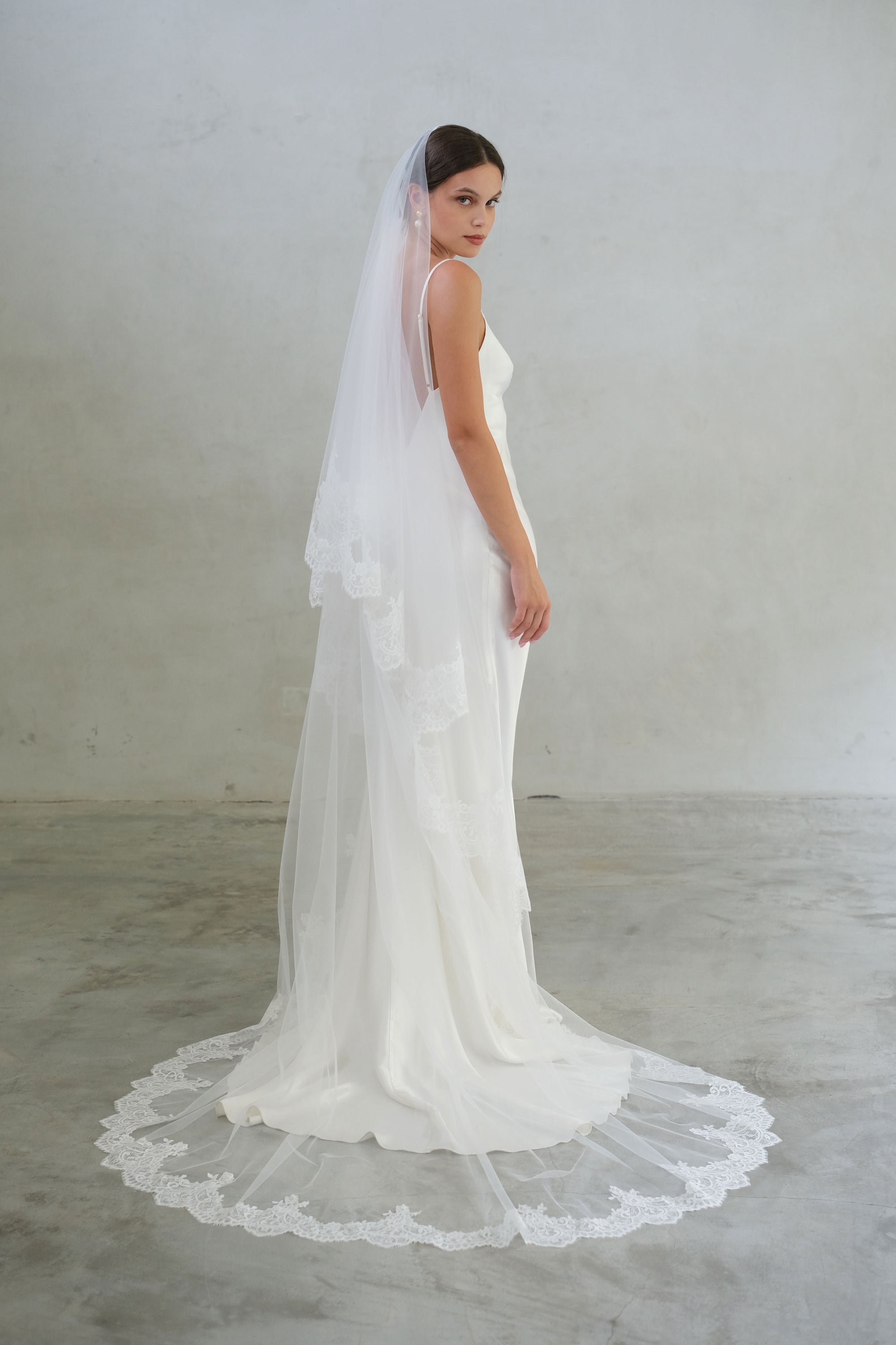 Full-length side profile of a bride wearing two-tier lace trim long modern wedding veil, blusher off