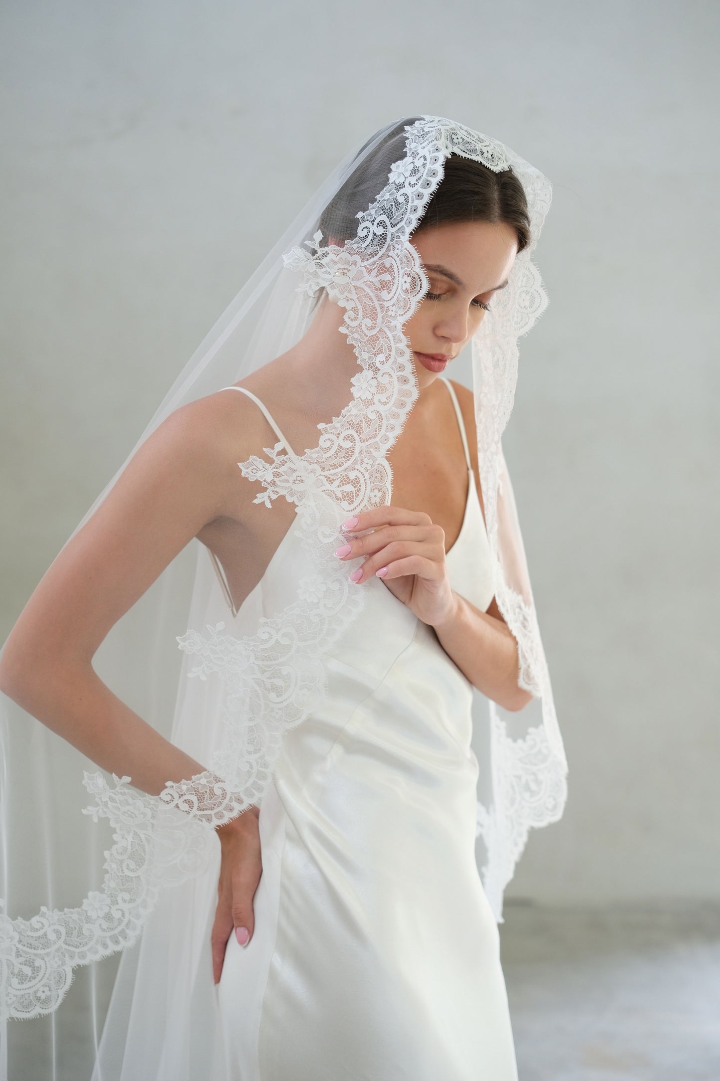 Bride holds lace of mantilla style wedding veil draped softly over hair and shoulders