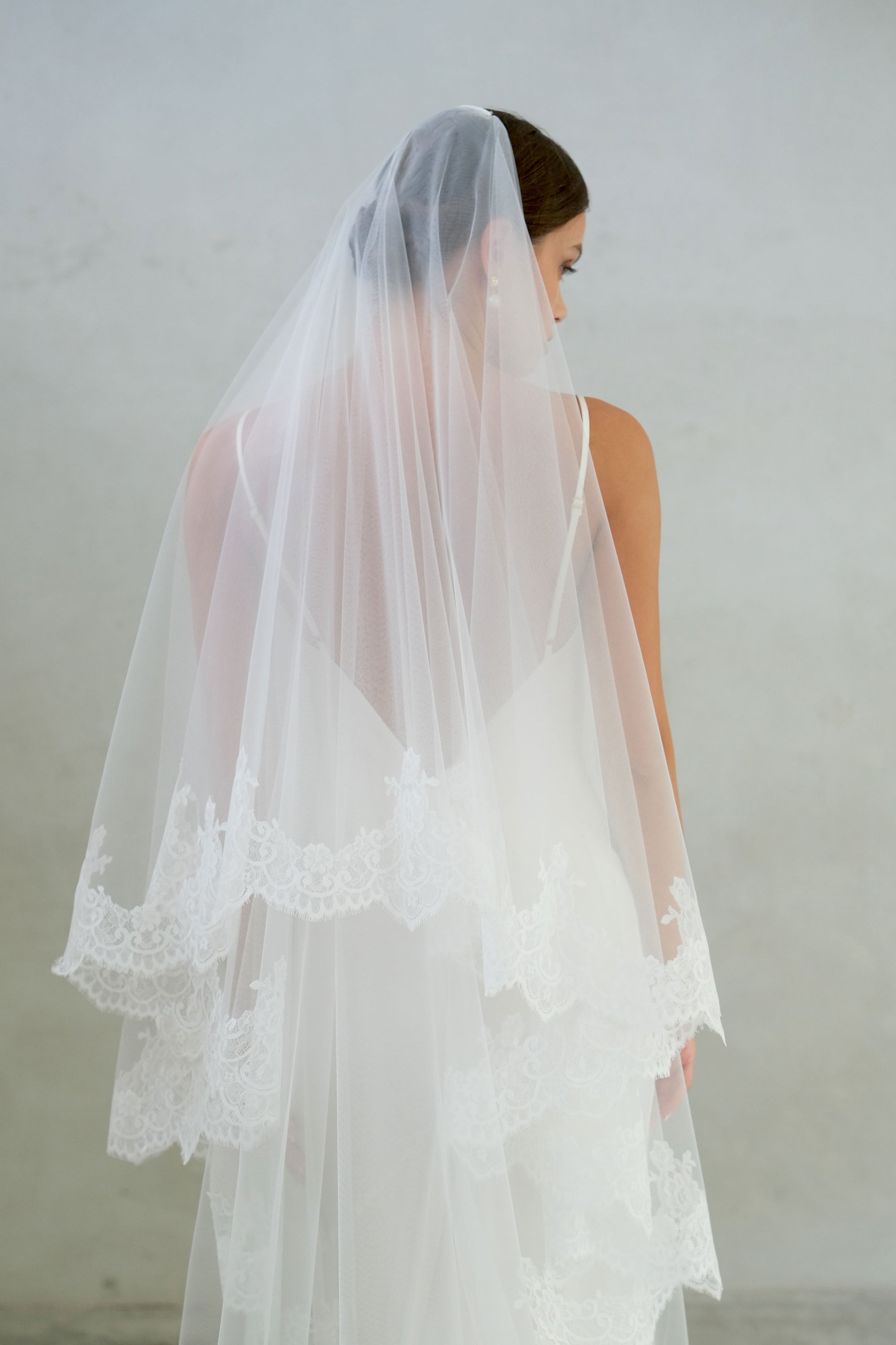 Half-length back view of a bride wearing two-tier lace trim wedding veil with blusher off