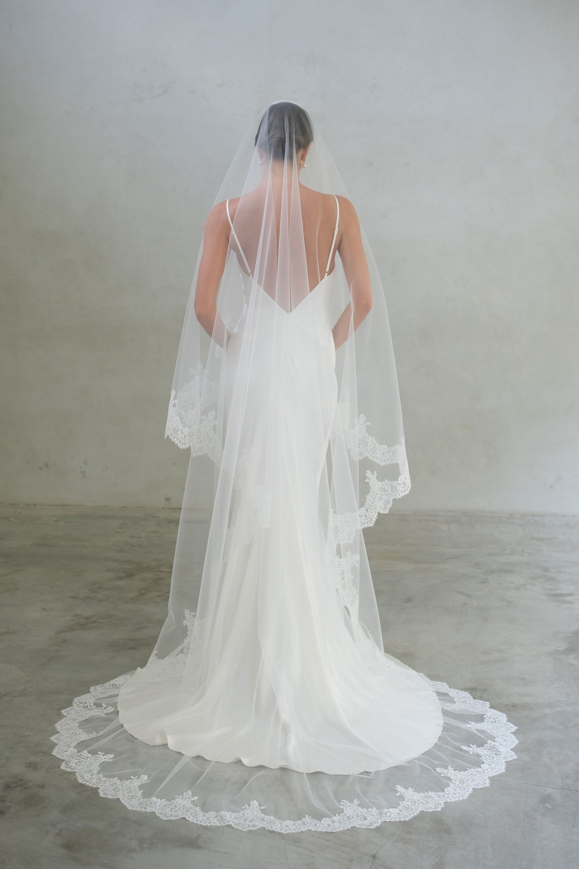 Full-length back view of a bride wearing two-tier lace trim long modern wedding veil with blusher in chapel length