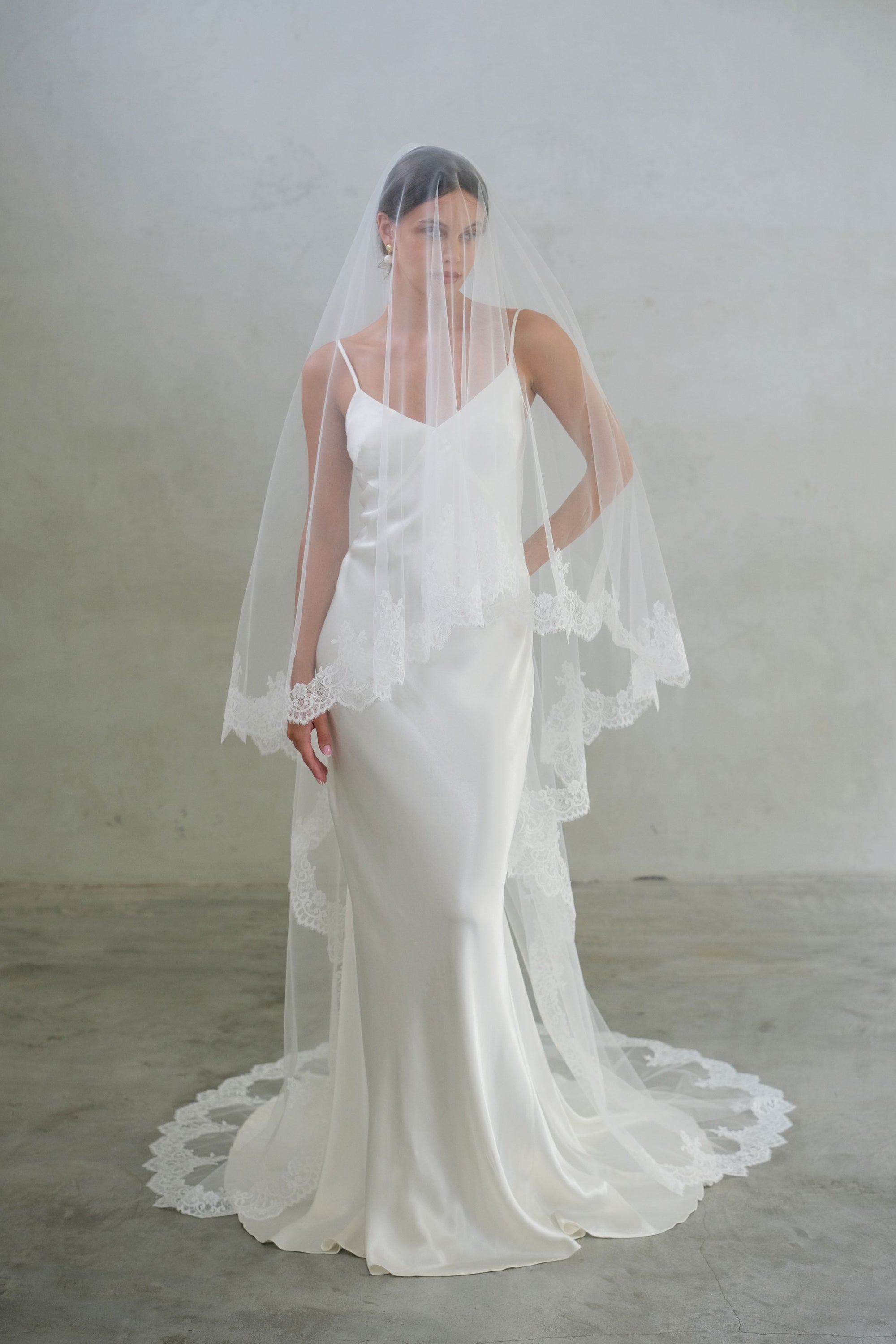 Full-length front facing bride wears two-tier chapel length wedding veil with lace edge, blusher down