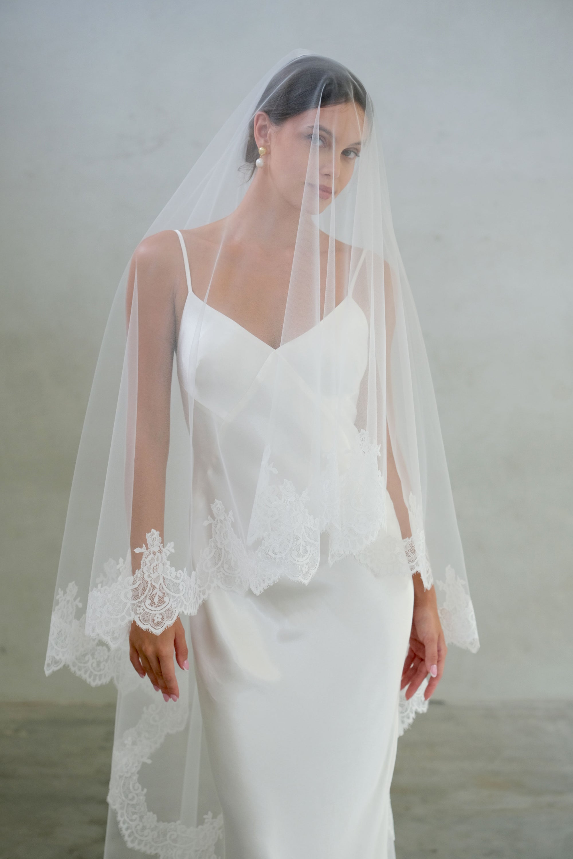 Half-length front-facing bride wears two-tier wedding veil with lace edge, blusher down