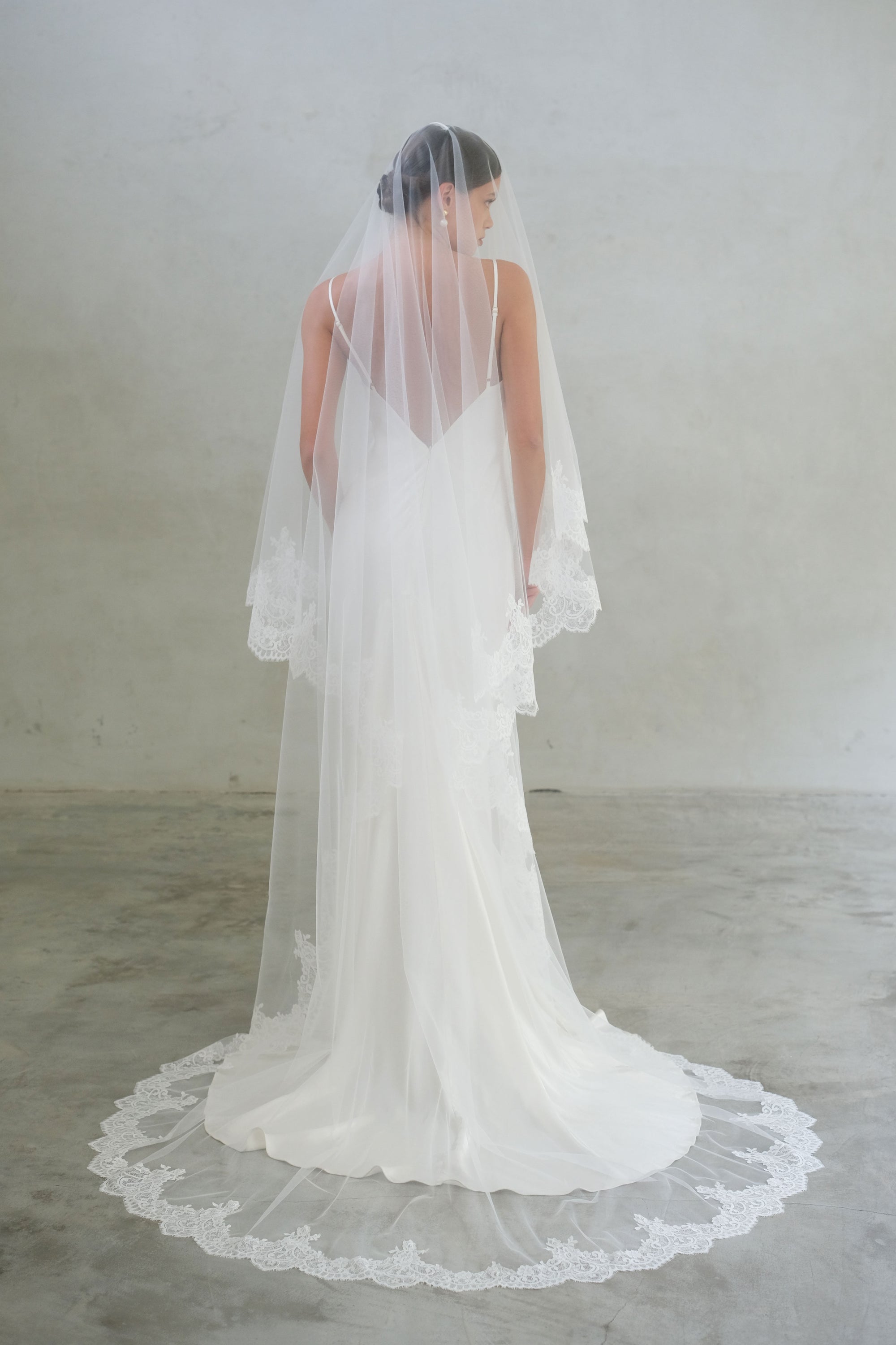 Full-length back view of a bride wearing two-tier lace trim modern wedding veil in chapel length with blusher