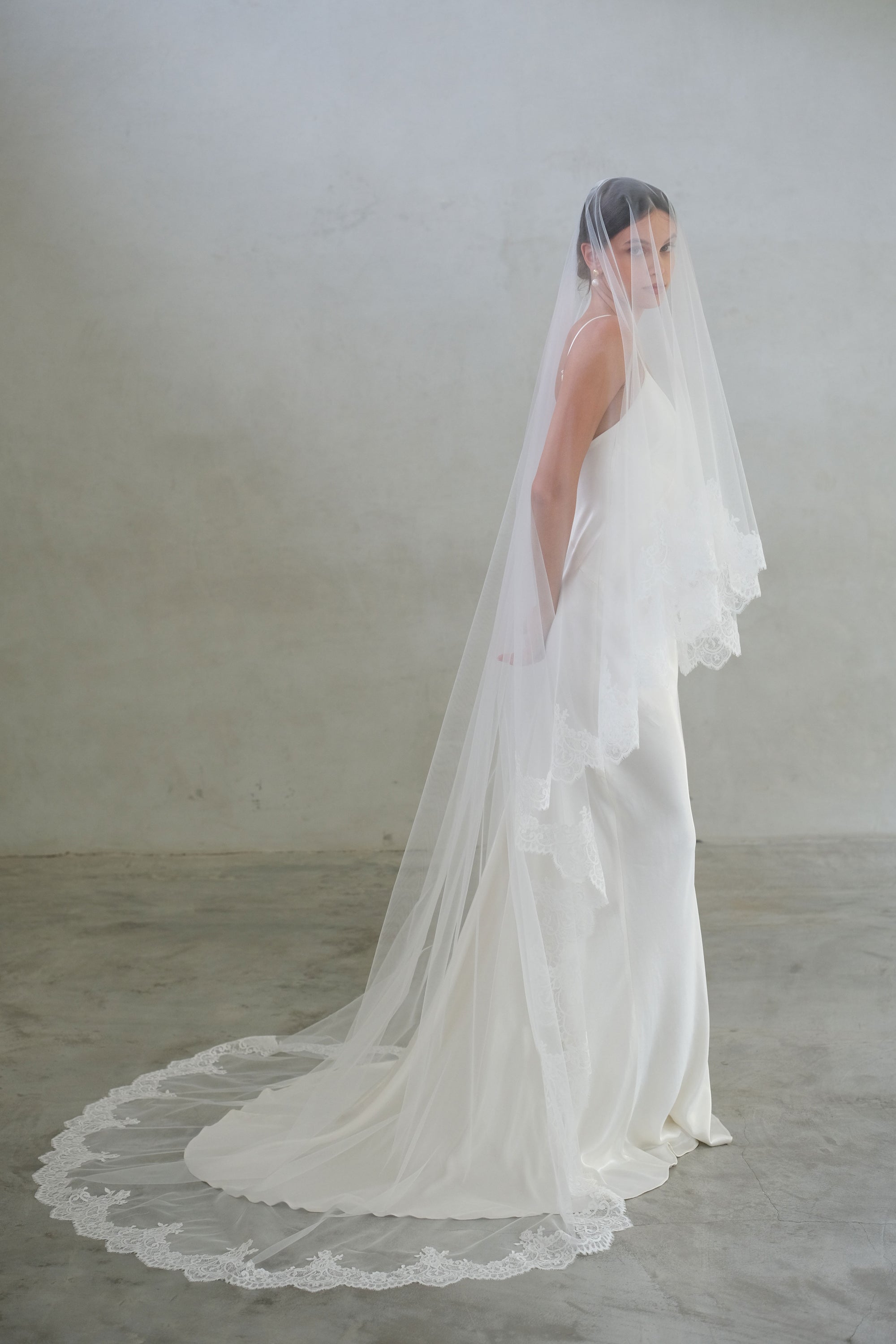 Full-length side view of a bride wearing long, two-tier modern wedding veil with lace trim
