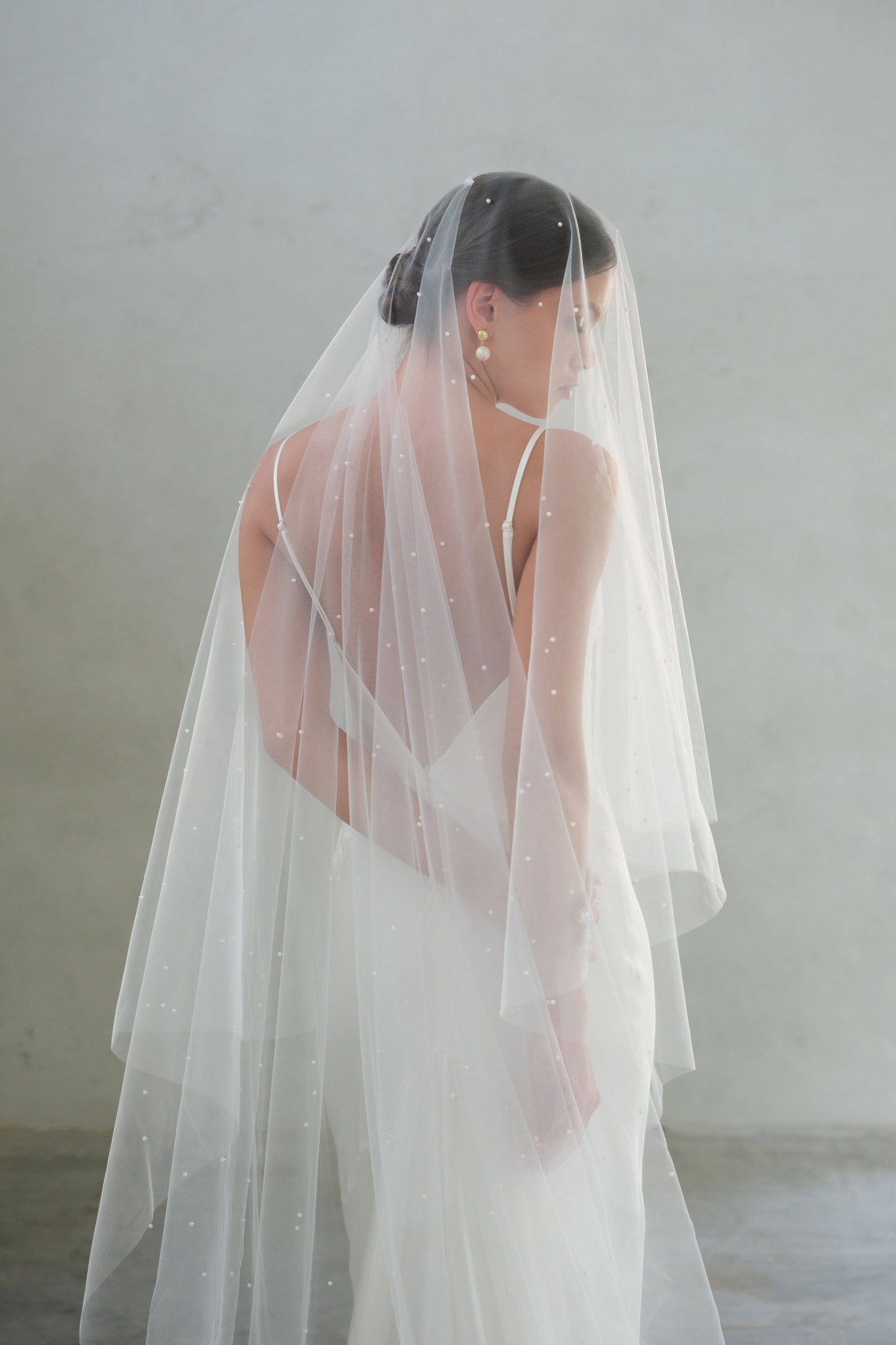 Half length back view of bride wearing two-tiered wedding veil showing scattered pearl detail