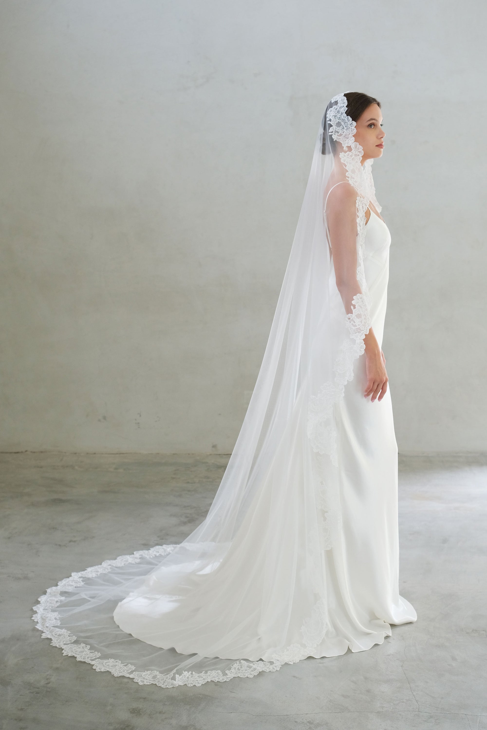 Full length side view of bride wearing long, lace trimmed veil in mantilla style