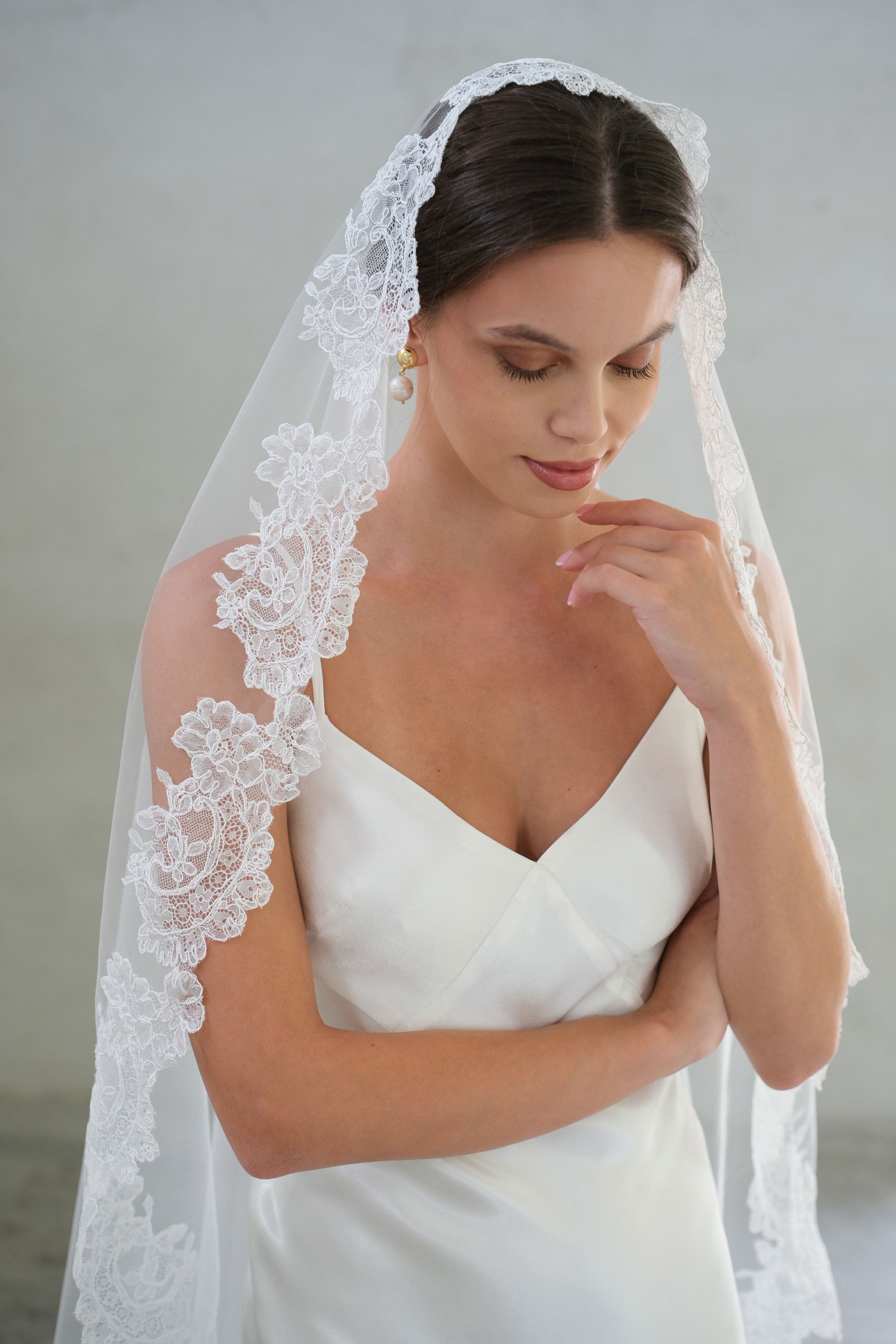 Floral lace trimmed bridal veil drapes over hair and shoulders of demure bride